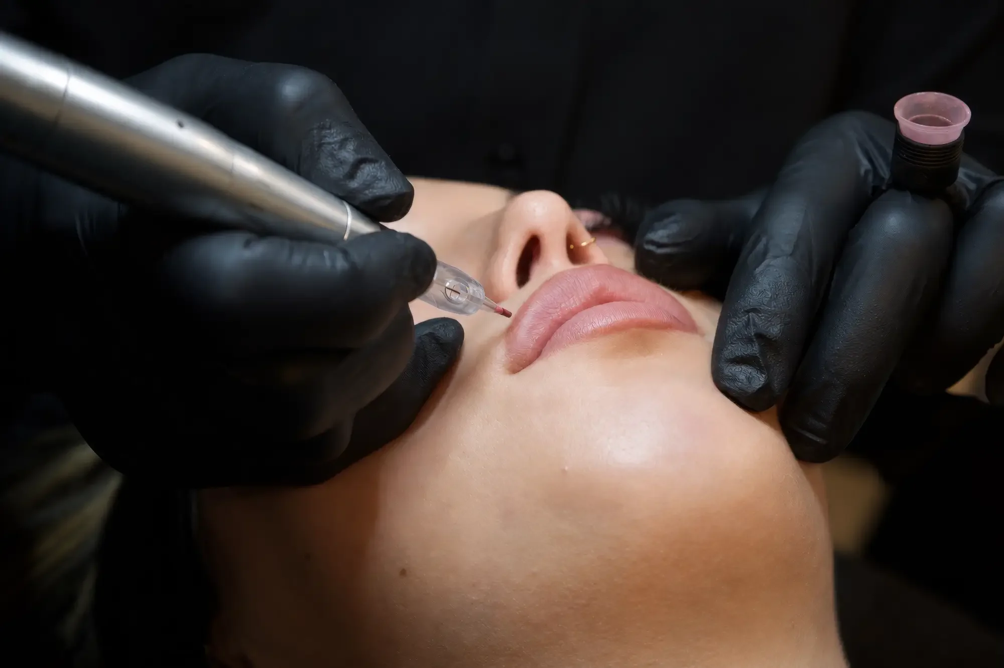 Ein Gesicht wird mit einer Tattoo-Maschine von einer Person in schwarzen Handschuhen tätowiert.