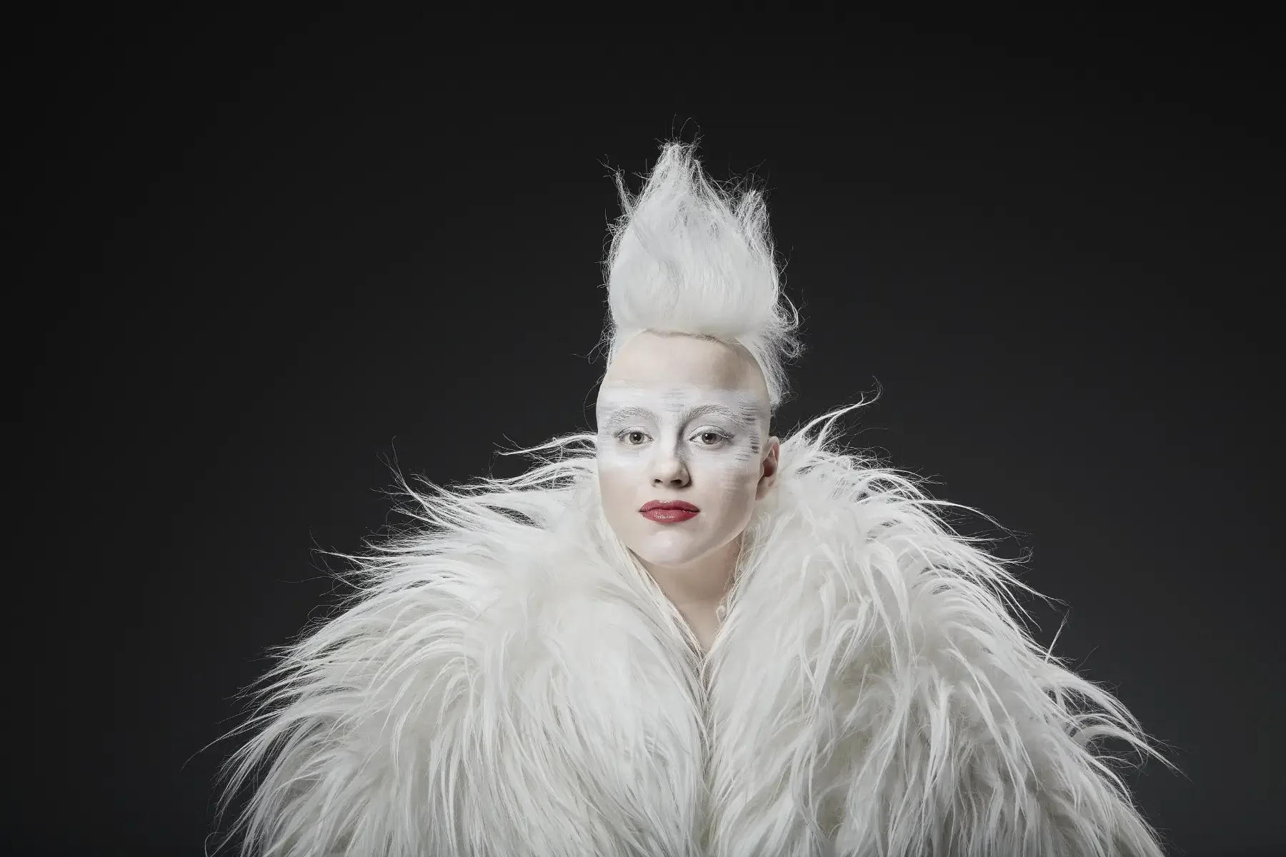 Zentral aufgenommenes Avantgarde-Porträt aus der Black-&-White-Fotoaktion mit weißem Haarstyling, textiler Körperinszenierung und kontraststarkem Make-up vor dunklem Hintergrund bei Garzareck in Halle (Saale).