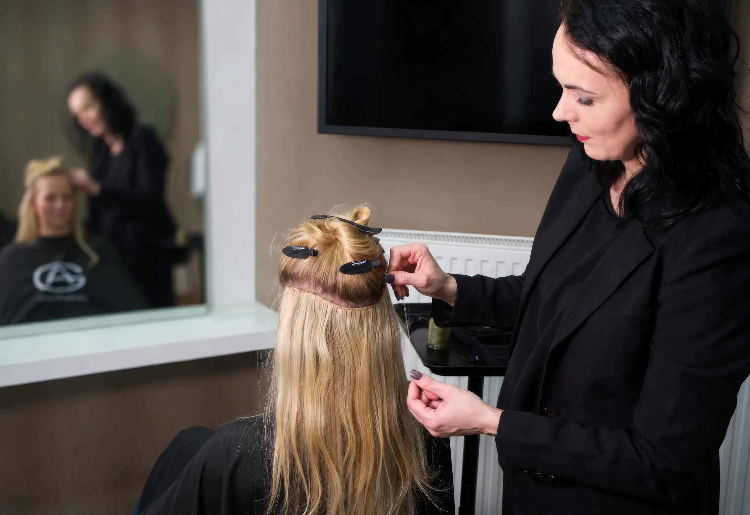 Friseur schneidet und stylt die Haare eines Kunden in einem Salon, während eine andere Person im Hintergrund beschäftigt ist.