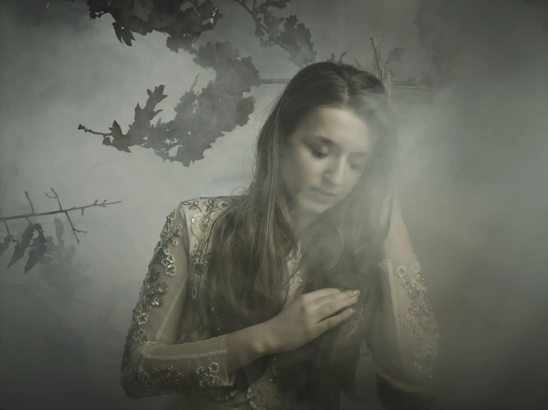 Model mit langen, dunklen Wellen und transparent besticktem Kleid in einer nebeligen Waldkulisse. Das ruhige Editorial-Porträt wirkt verträumt, natürlich und atmosphärisch inszeniert.