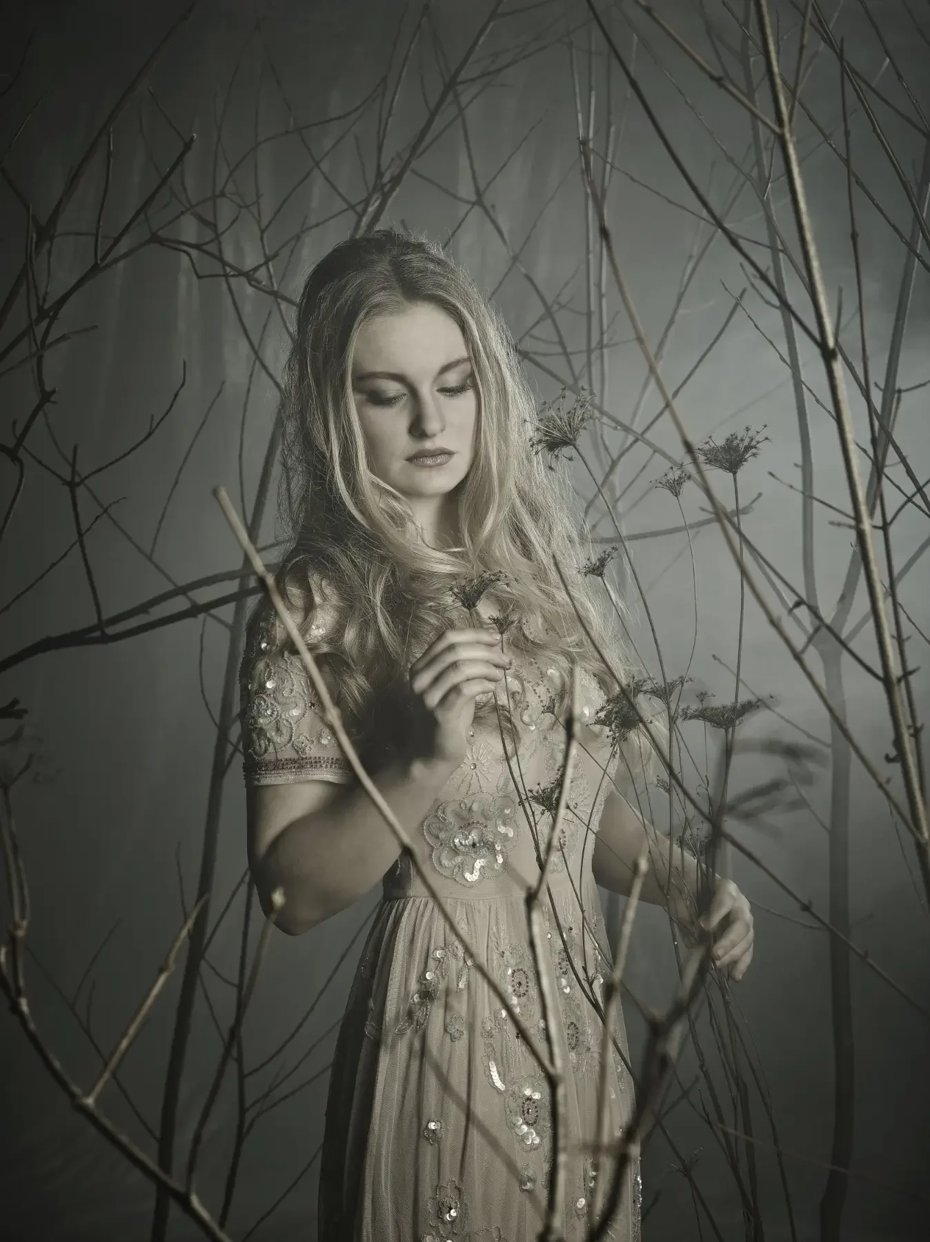 Blondes Model mit sanfter Wellenfrisur und besticktem Kleid zwischen feinen Ästen in einer nebeligen Waldszene. Das naturinspirierte Editorial verbindet Hair Art und ruhige Avantgarde-Fotografie von Garzareck Halle.