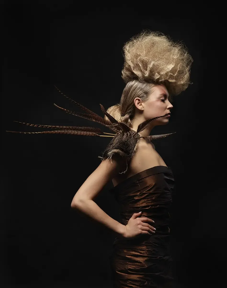 Studio-Porträt mit skulpturaler Hochsteckfrisur, schwarzer Couture und naturinspiriertem Schulterobjekt vor dunklem Hintergrund.