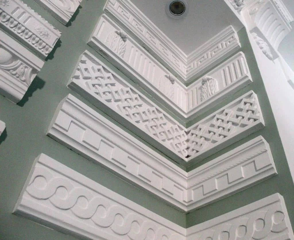 Muestrario de molduras decorativas blancas con diversos patrones arquitectónicos. Incluye diseños con motivos geométricos, lineales y ornamentales.