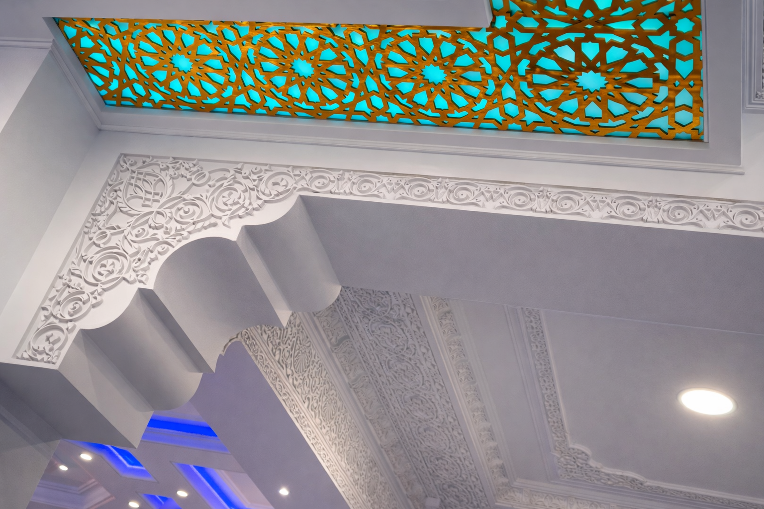 Detalles decorativos en el techo con patrones de yeso en relieve y una vitral con diseño geométrico en tonos azules y dorados.