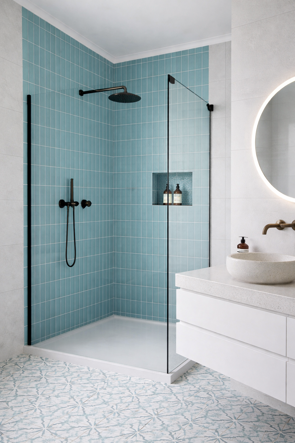 Baño con ducha de azulejos azules, pared de espejo redondo con luz LED, lavabo de piedra y accesorios en tono bronce.