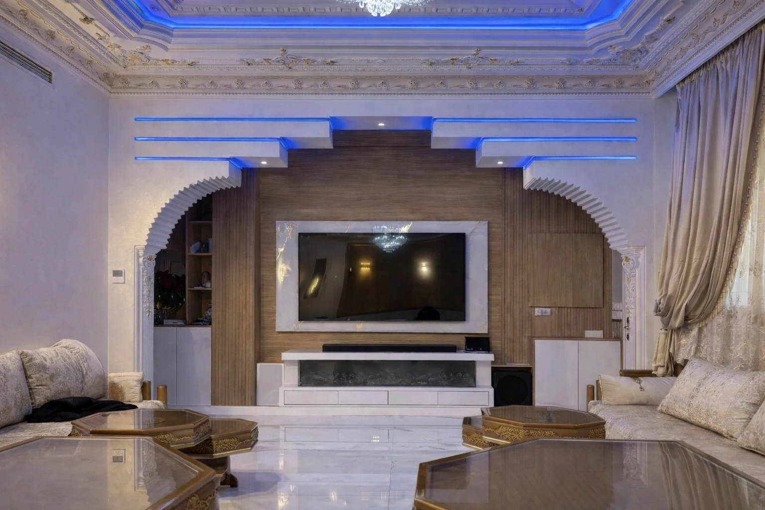 Sala de estar con pared de madera y televisor de pantalla plana, sofá beige y mesas de madera, cortinas doradas y cielo con iluminación LED azul.