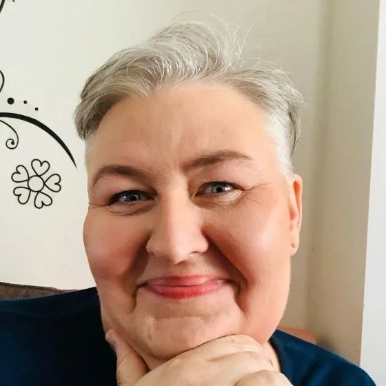 Close-up of a smiling woman with short gray hair, resting her chin on her hand
