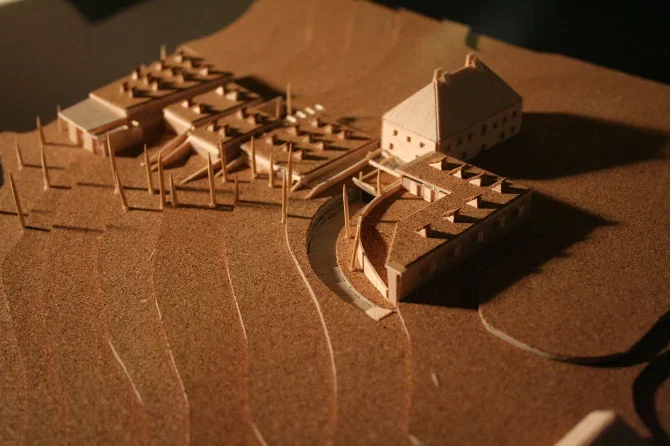 A detailed architectural model of a building complex on a sloped terrain, including multiple structures and pathways.