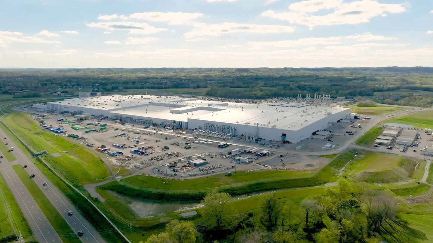 Aerial view of the Colossus datacenter by Elon Musk with a parking lot, trucks, and green landscape.