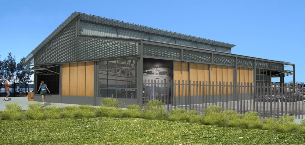 A modern, two-story building with a metal and wood exterior, surrounded by a fence and greenery, with people walking nearby.