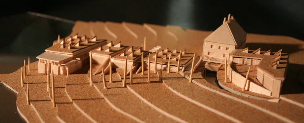 Architectural model of a building complex on a sloped terrain with terraced landscaping and a detached building in the background.