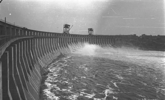 Black and white photo of the Kakhovka hydroelectric dam in Ukraine with water flowing over the edge.