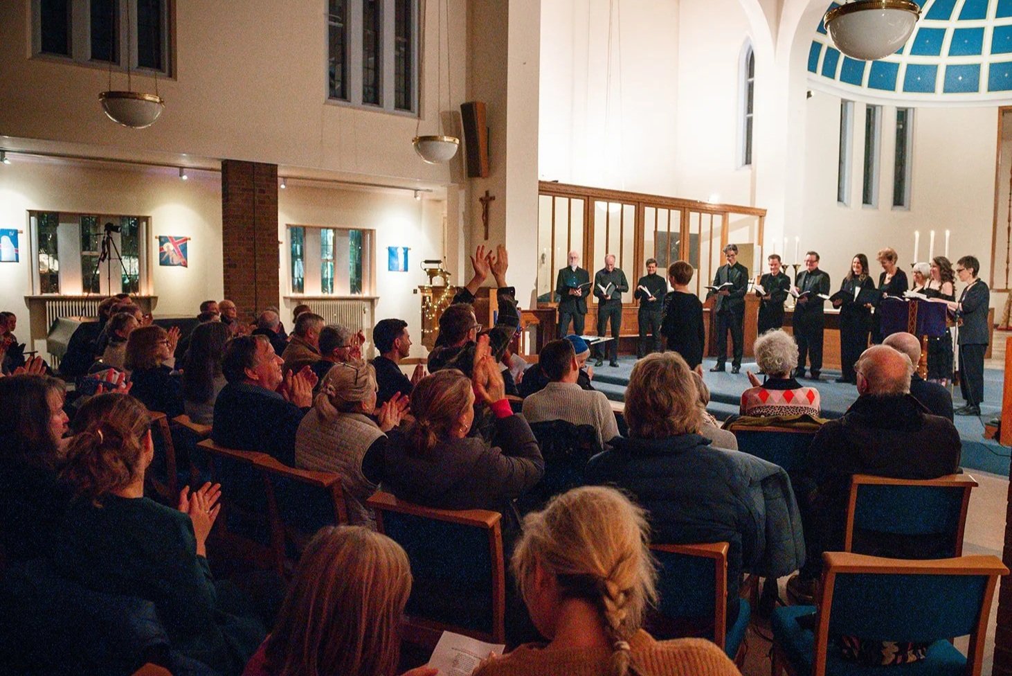 Audience members applauding heartedly during a performance in a church, with brick pillars and artwork on the walls.
