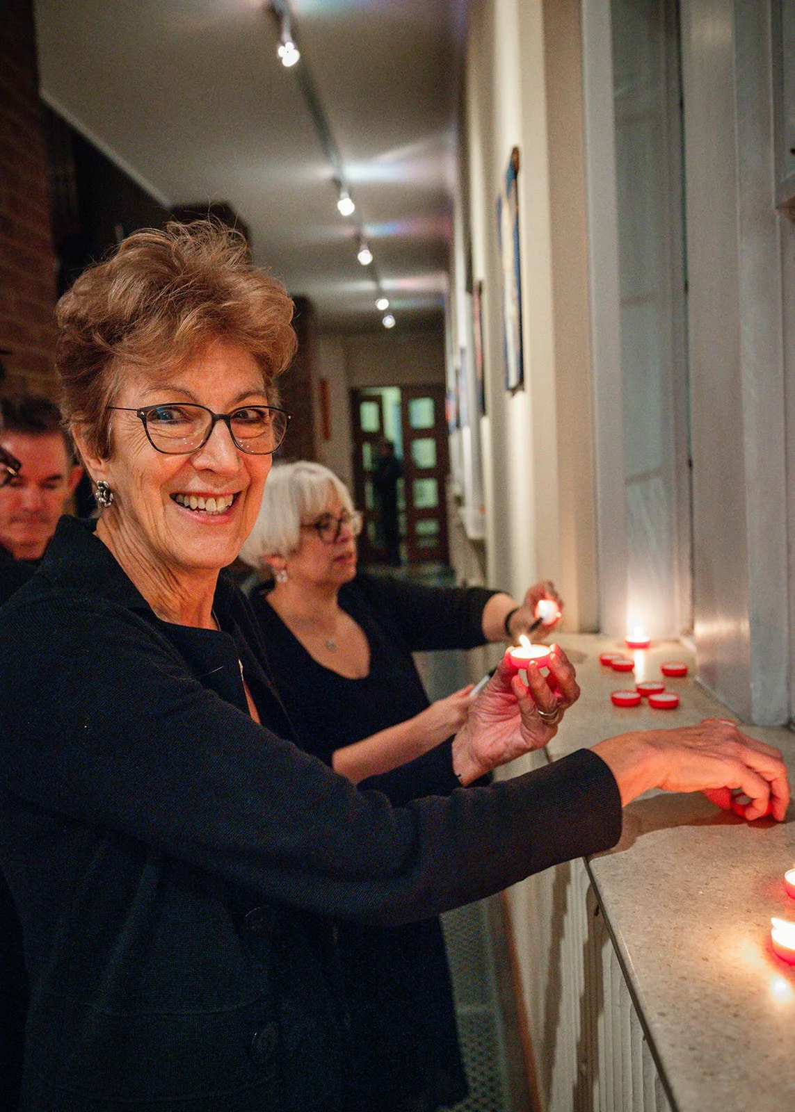 Two women preparing for an event by lighting candles on a windowsill.