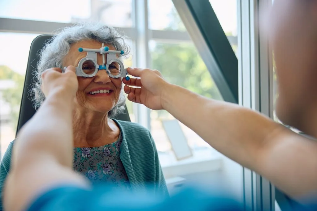 A senior woman being fitted for glasses by an optometrist in an eye exam room.