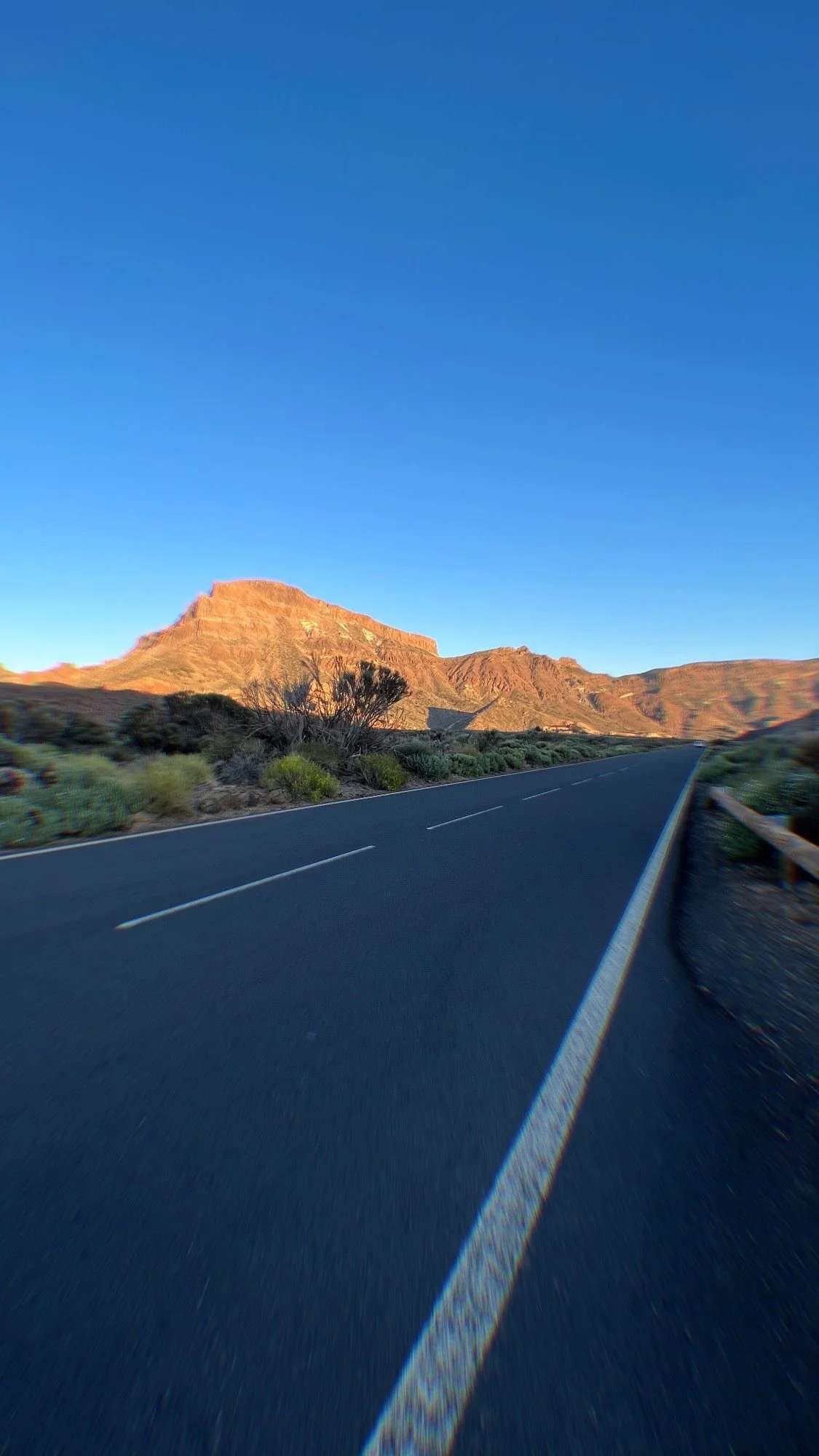 Une route sinueuse dans un paysage désertique avec des montagnes en arrière-plan et un ciel clair et bleu.