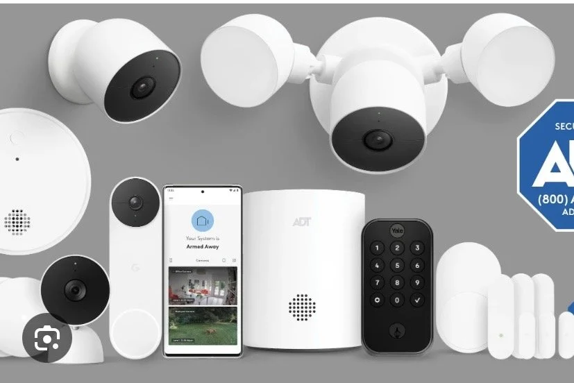 Home security system components on a gray background, including cameras, a control panel, a remote, a motion detector, a door/window sensor, and a smartphone showing app interface.