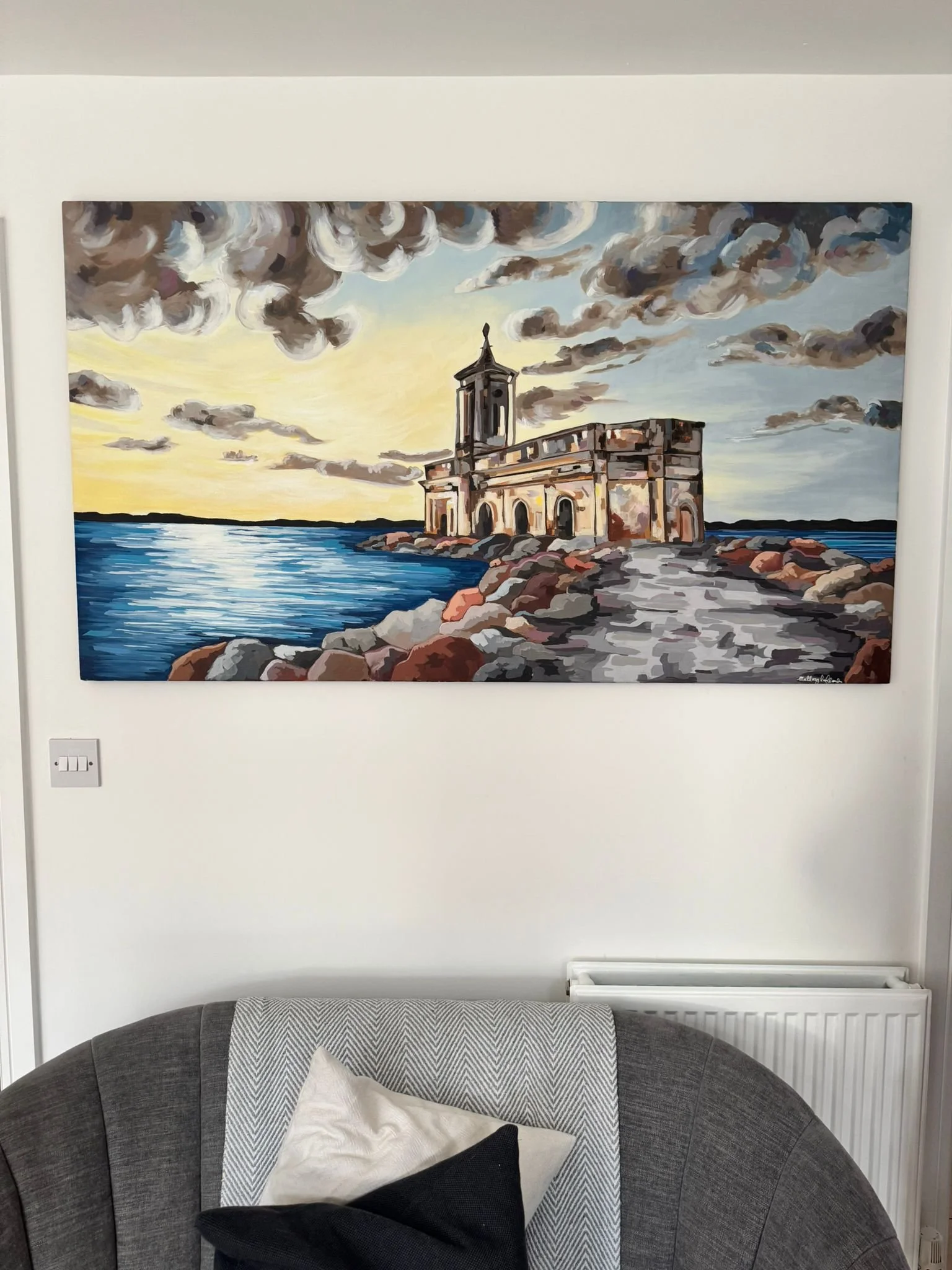 Painting of a lighthouse by the water at sunset with dramatic clouds overhead.