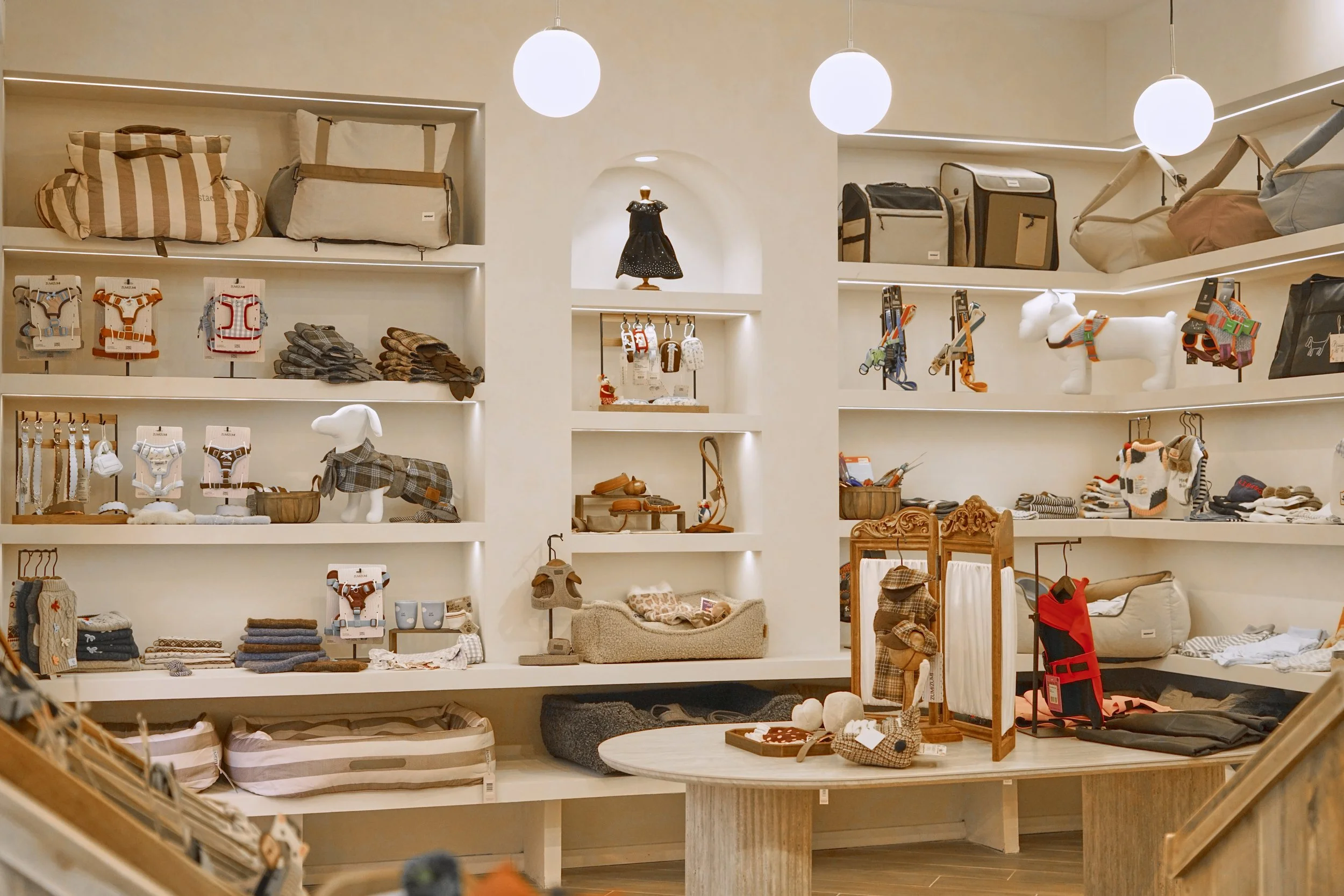 Scaffale di negozio con accessori e abbigliamento per cani, tra cui guinzagli, cappotti, collari, giochi, e altri oggetti, in un ambiente ben illuminato.