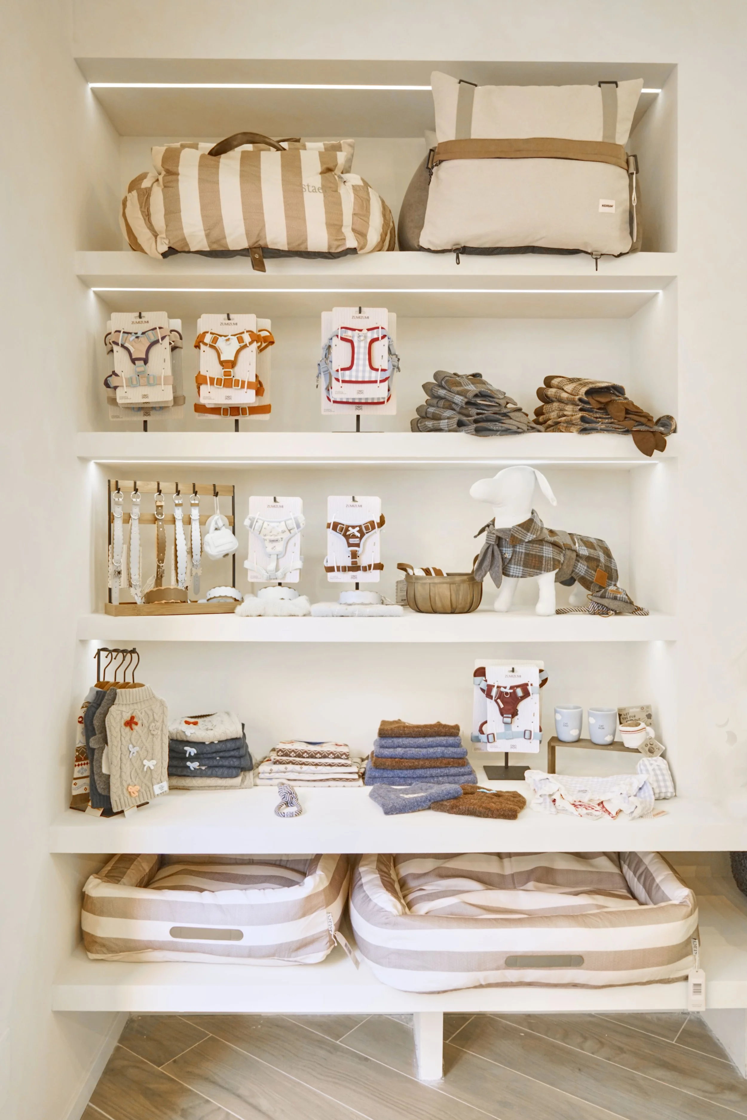 Scaffale di prodotti per animali domestici, con vestiti, accessori, lettini e borse in stile neutro e cottagecore.