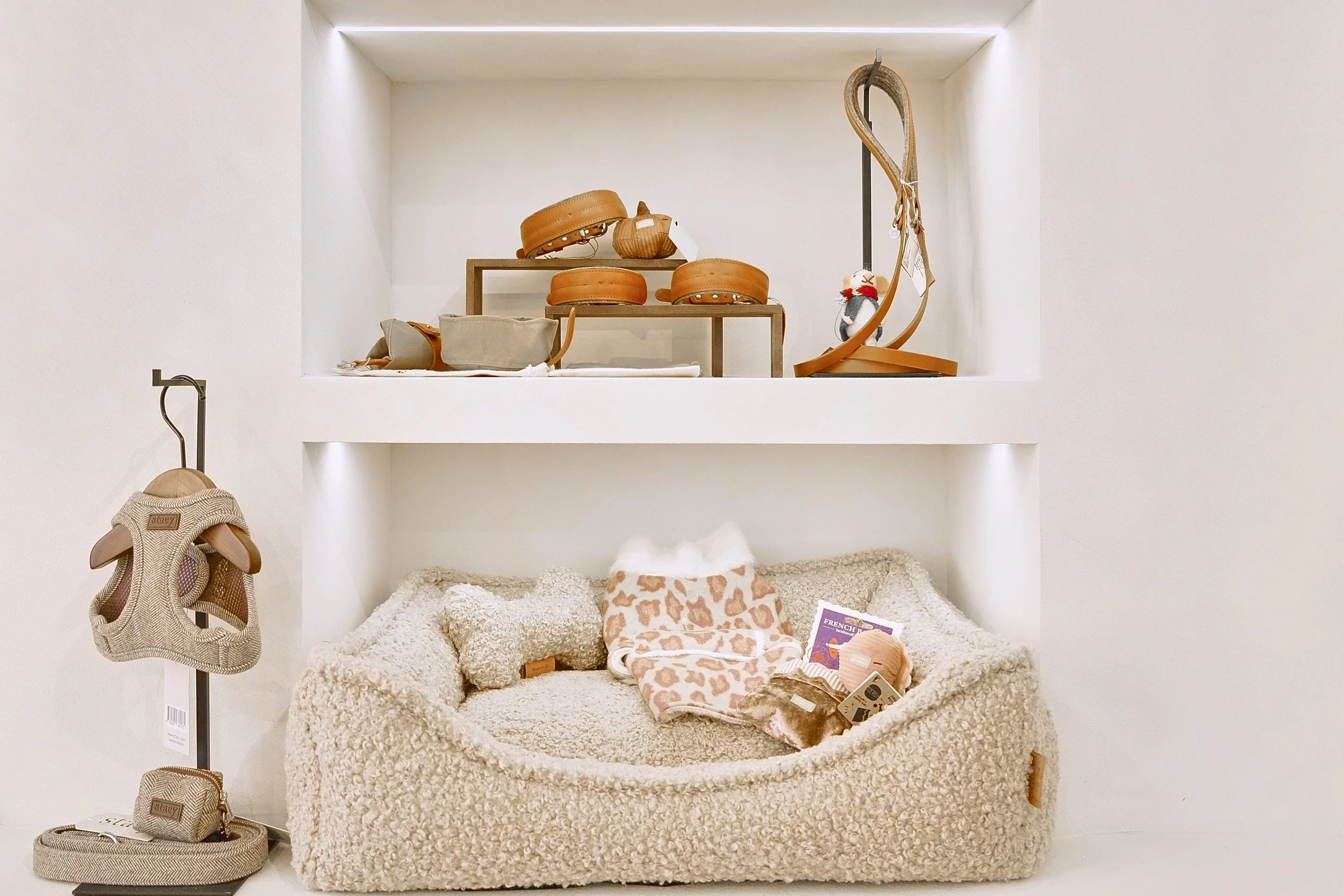 Una scatola con vari accessori per animali, come abbigliamento e guinzagli, in una vetrina con scaffali e un'area morbida per animali domestici.