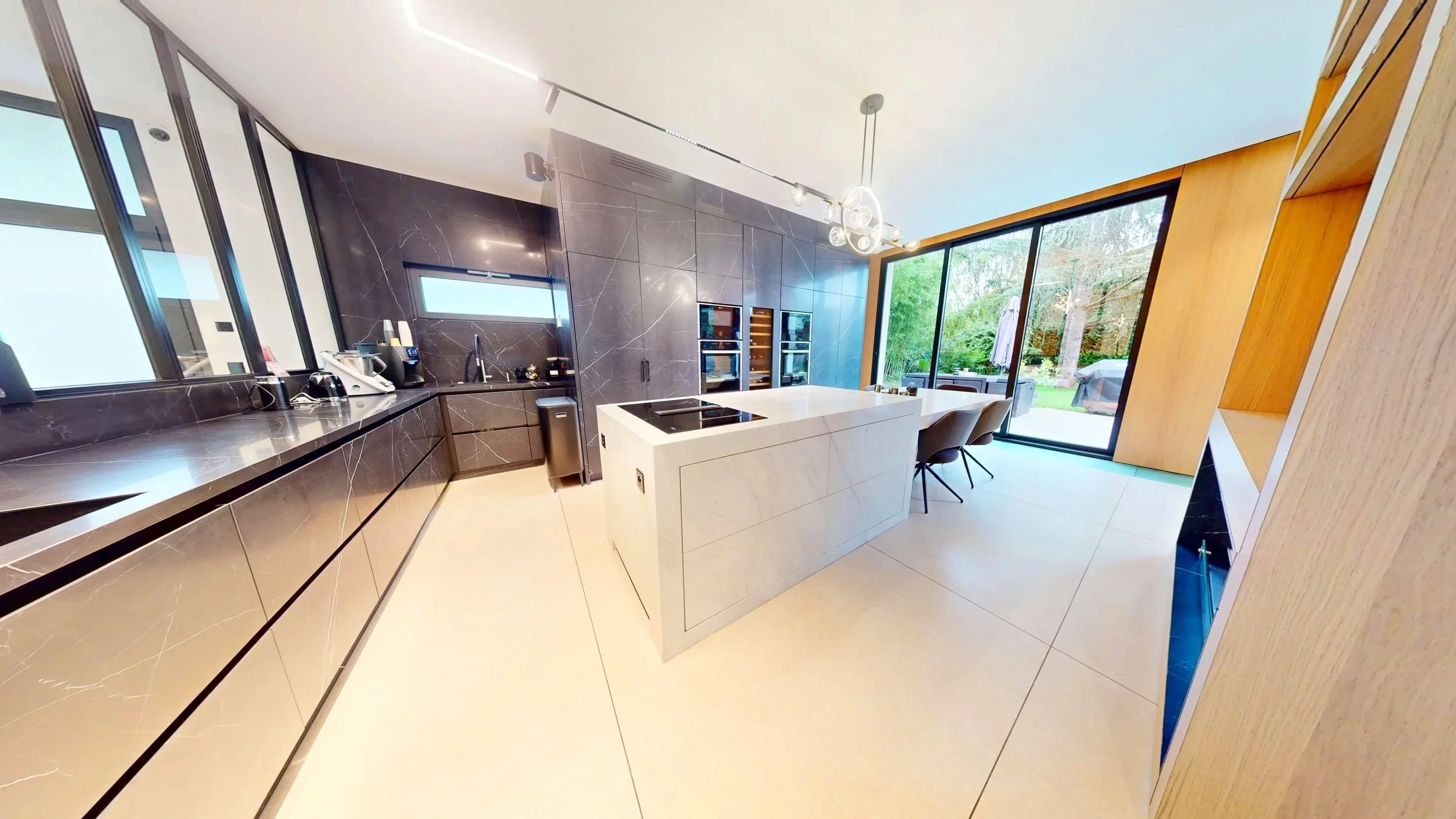 Cuisine moderne avec îlot central en marbre blanc, murs en marbre noir, grande vitre donnant sur un jardin et mobilier contemporain.