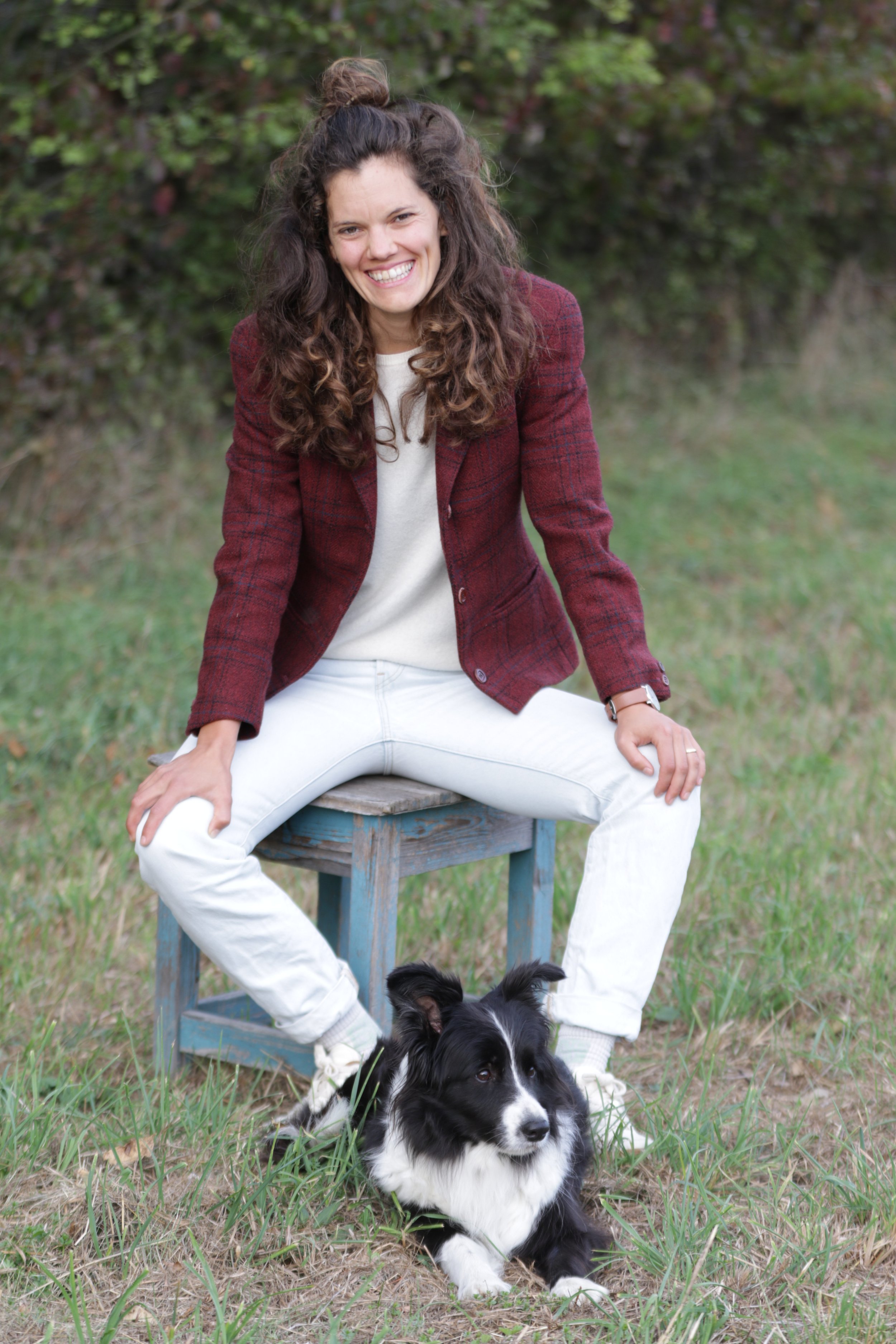 Lena Ramstetter sitzt auf einem Hocker auf einer Wiese, vor ihr liegt ein Border Collie