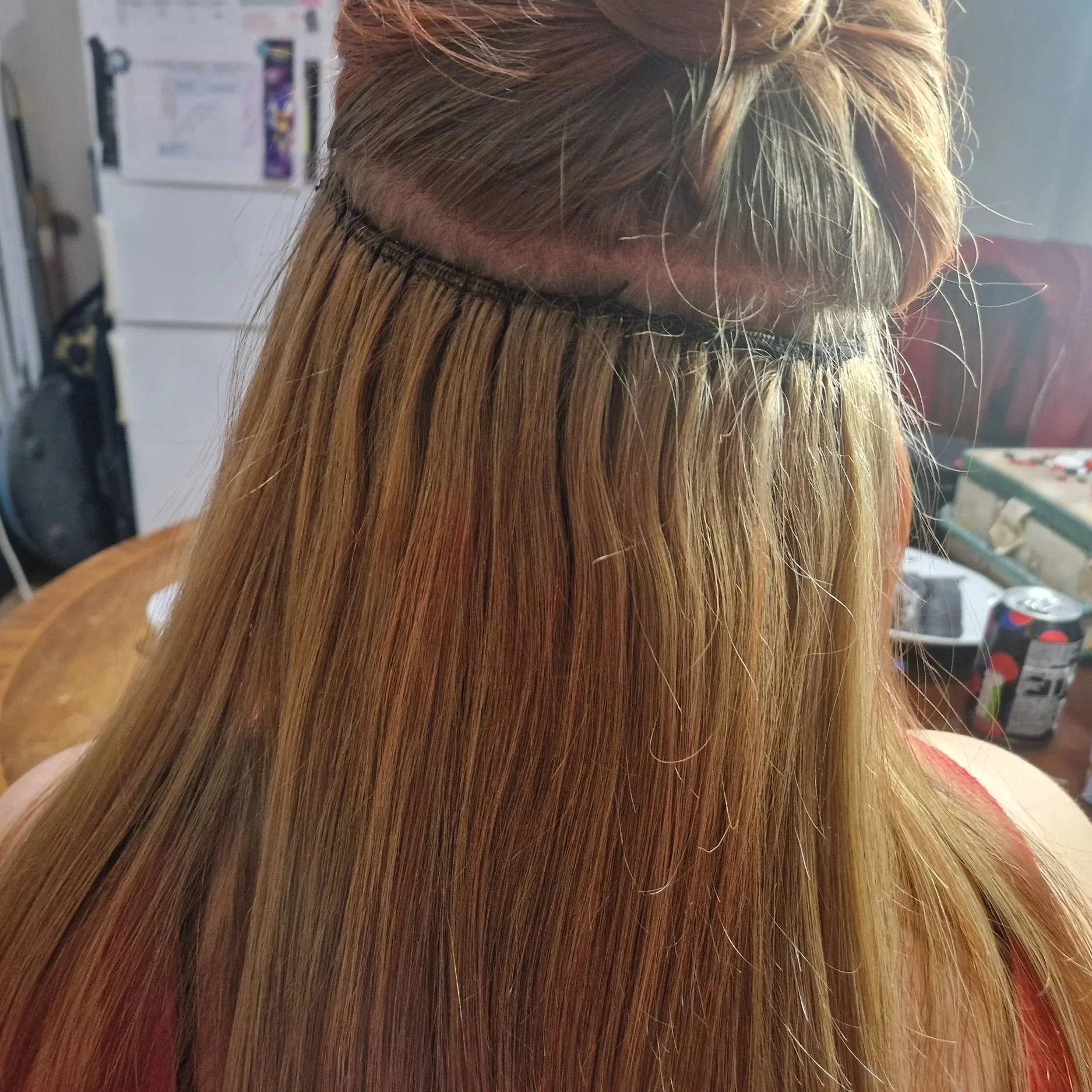 Close-up of a person with long, blonde hair being styled or processed, with a focus on the hair and a black headband or hair wrap. The background shows a refrigerator and various household items.