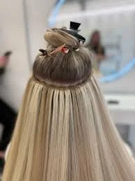 Hairdresser applying hair treatment or styling hair on a client with long blonde hair in a salon.