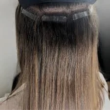Back of a person's head with straight, ombre hair transitioning from dark at the top to lighter at the ends, covered with a black hair salon cape.