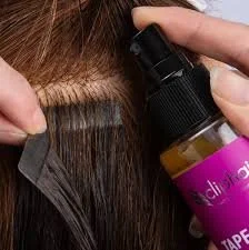 A person applying hair adhesive or tape to hair with a spray bottle nearby.