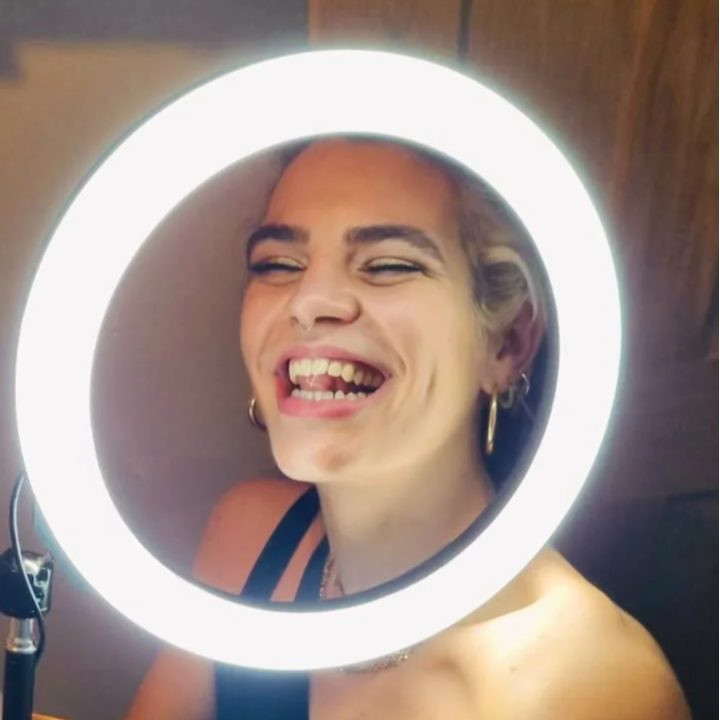 Person  (Lily the tattoo artist) smiling and laughing while looking through a round ring-light