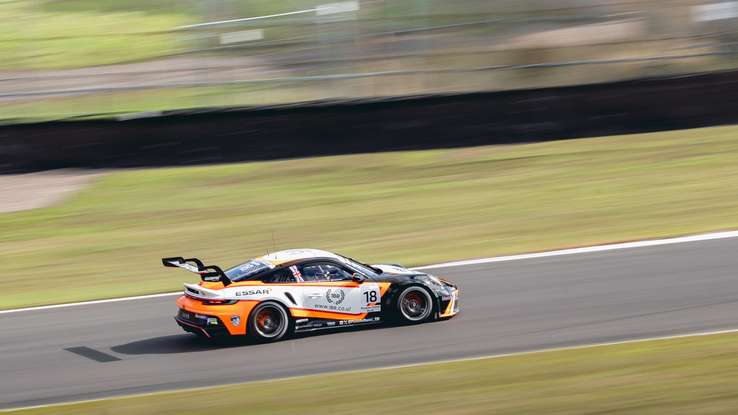 Race car on track with a black and orange design, numbered 18, speeding around a curve with blurred background