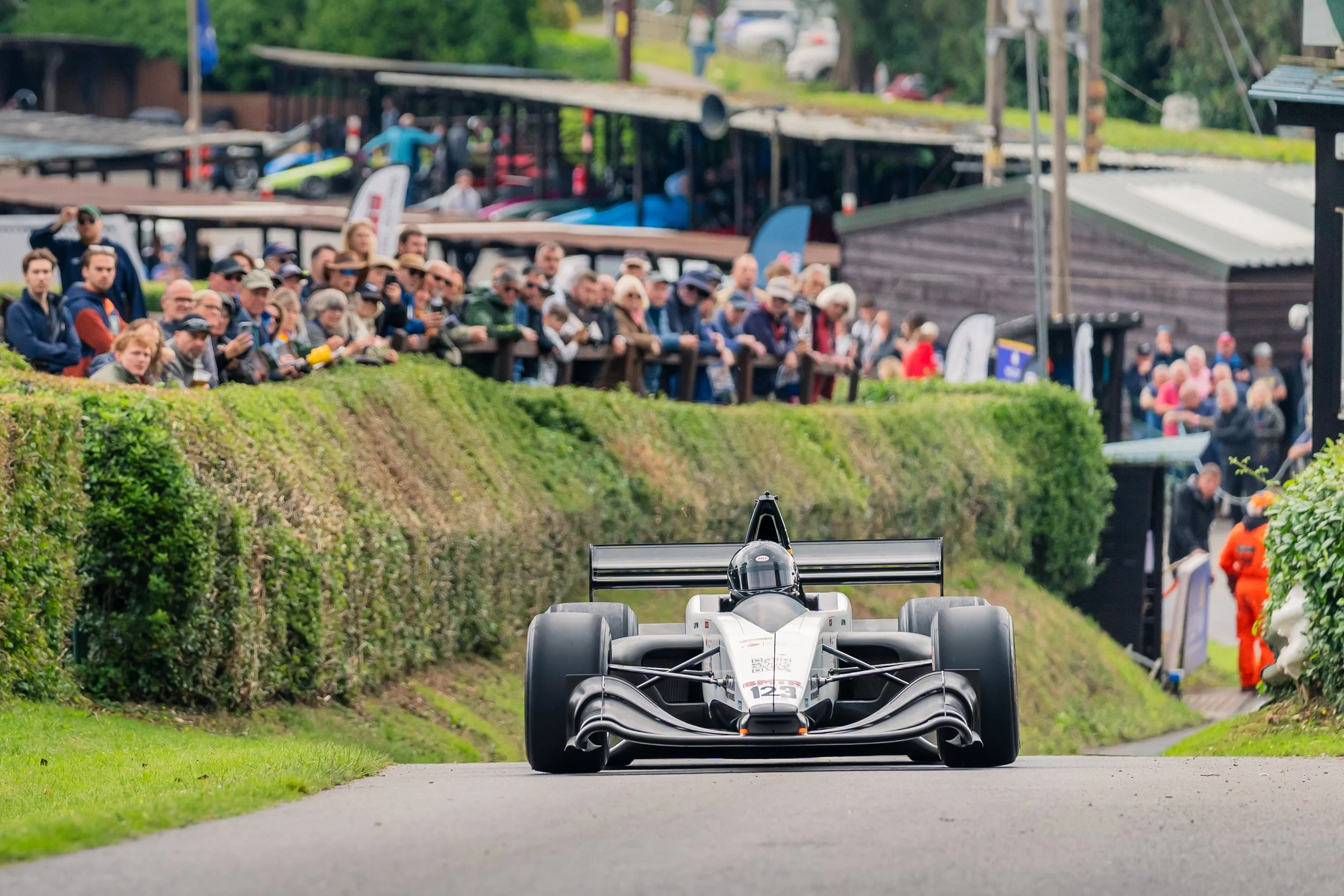 A race car driving down a track with spectators watching from a hillside along the side of the track.