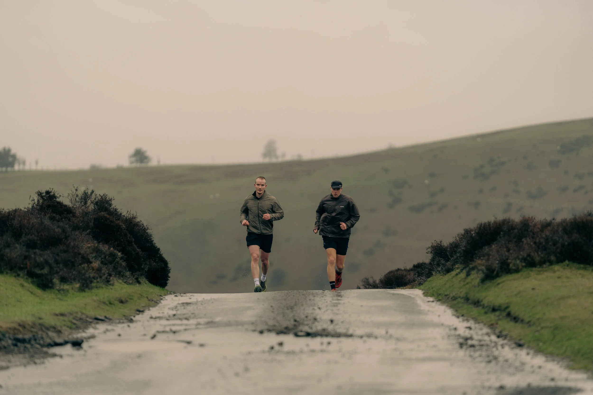 Two runners approaching along a misty hillside road for the Torra Performance Long Mynd campaign