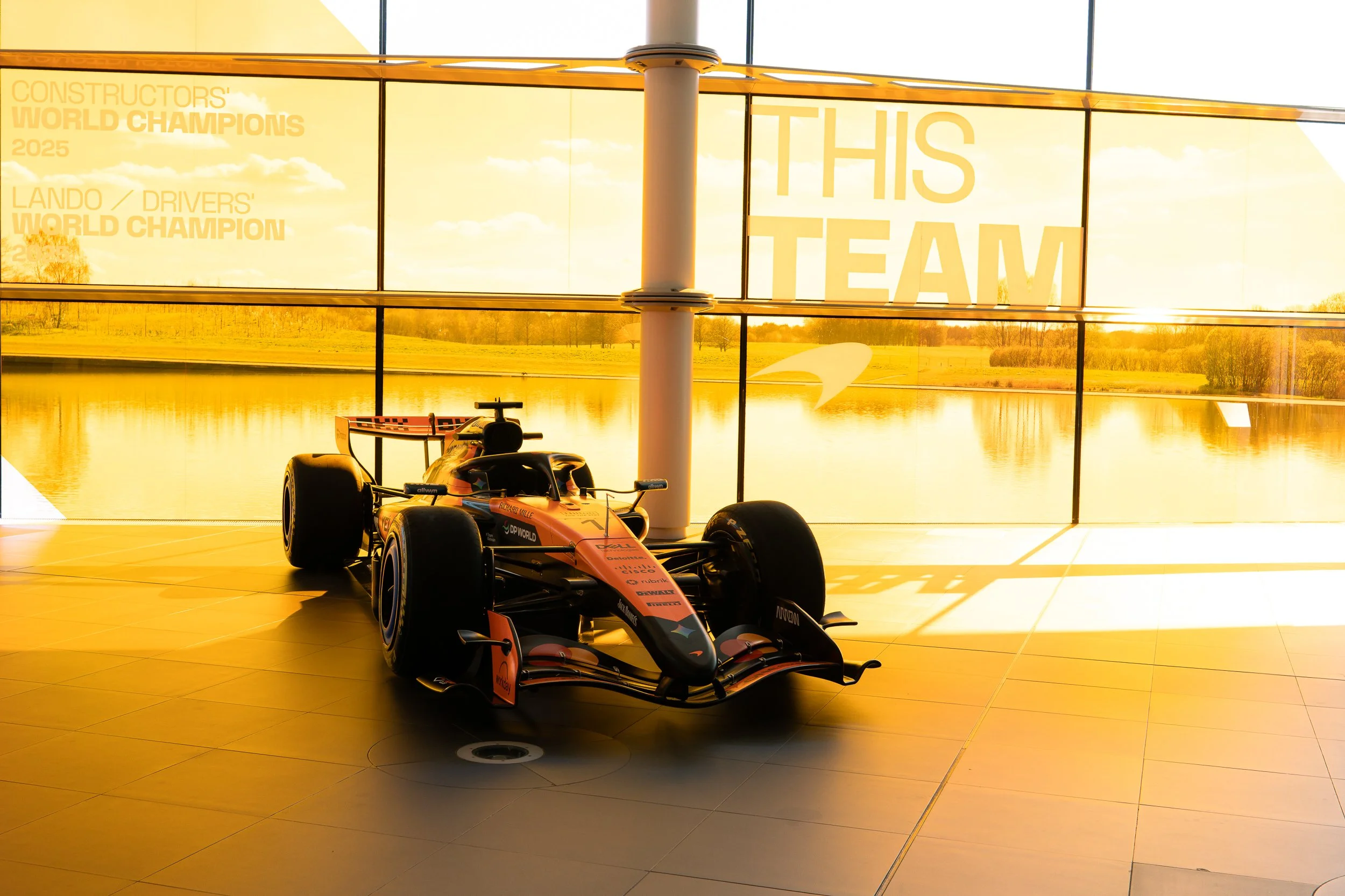McLaren Formula One car silhouetted against the lakeside windows at the McLaren Technology Centre