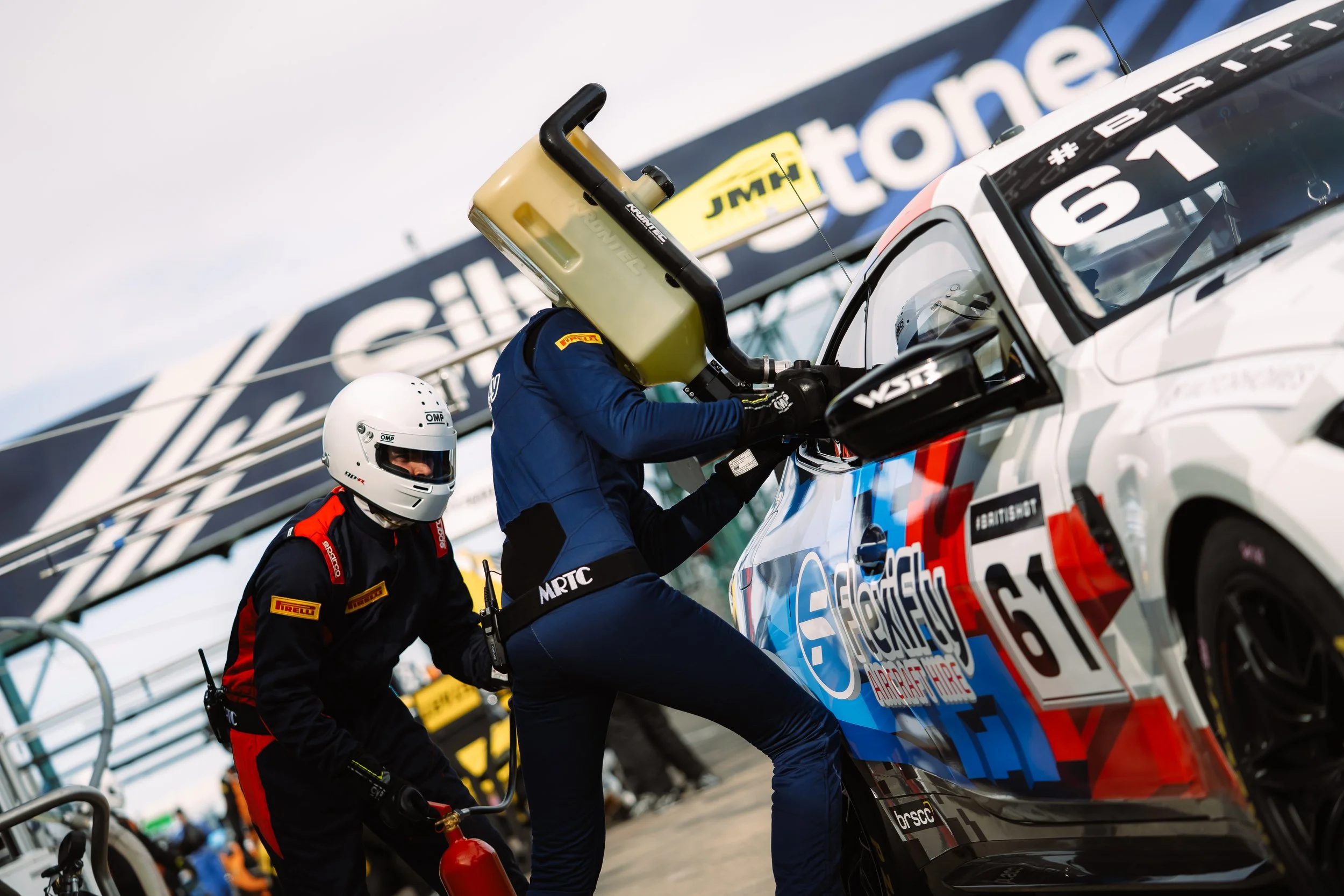 Race car pit stop with crew members changing tires and performing maintenance on a racing vehicle during a competition.