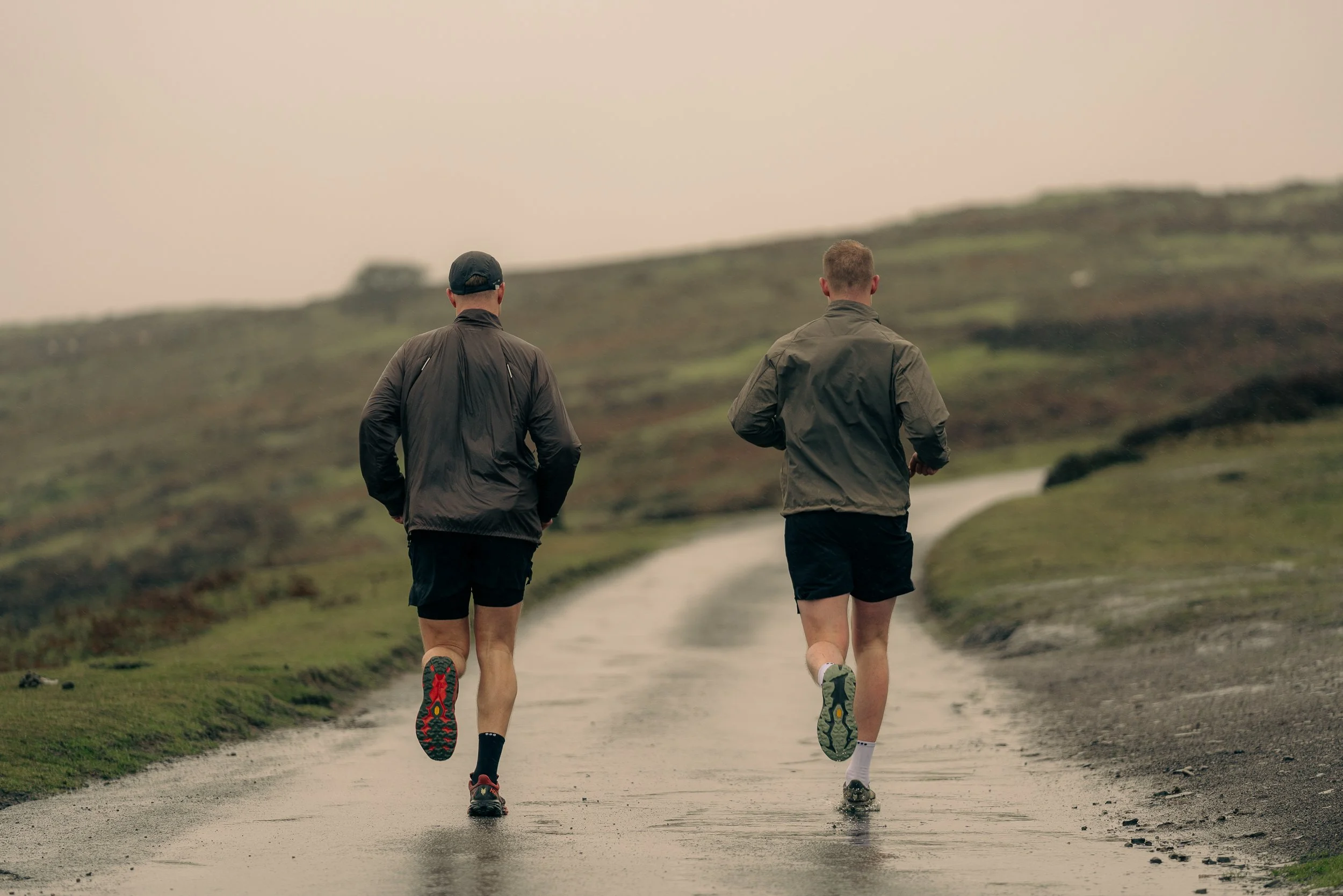 Two runners seen from behind running up a wet hillside road for the Torra Performance Long Mynd campaign