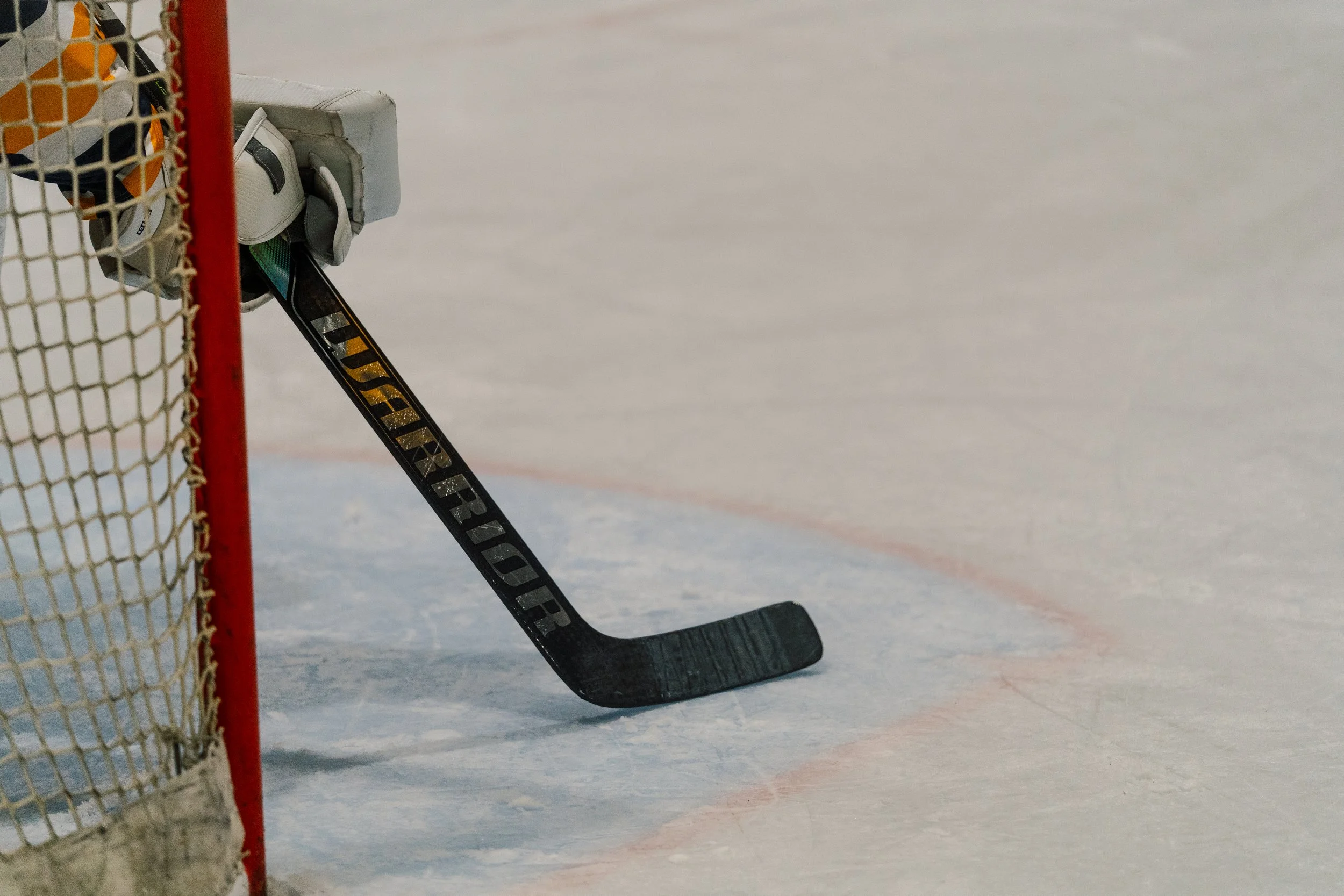 Close-up of a hockey goalie's skate blade next to the goalpost and net on the ice rink.