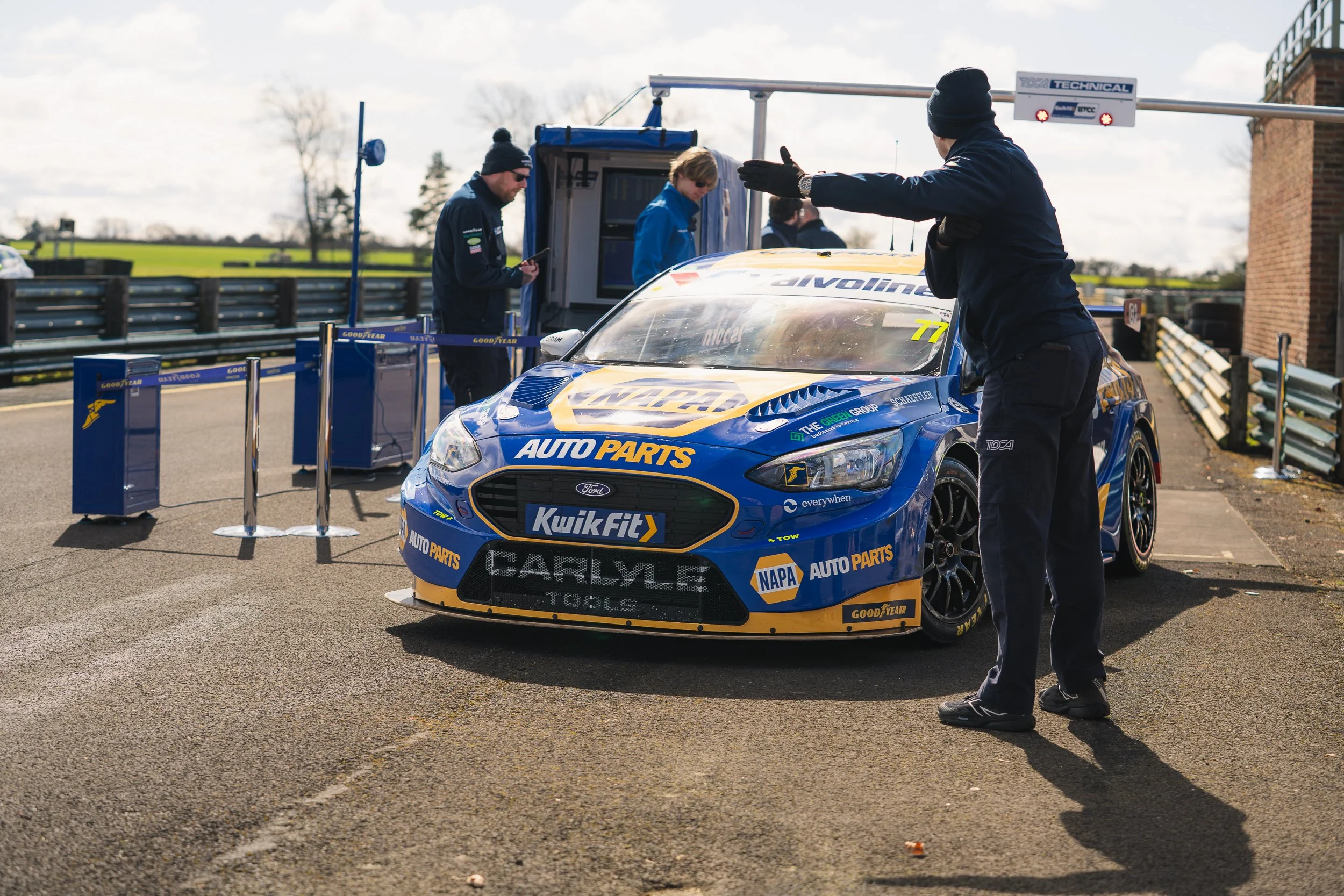 Crew pushing a blue Ford BTCC car through the pit lane gate at Croft testing