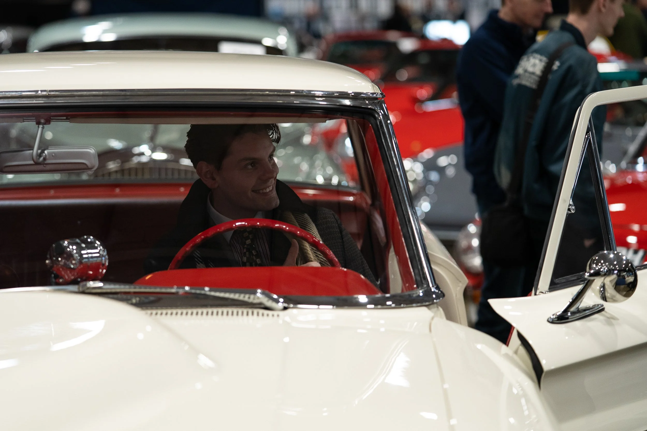 Driver seated in a classic cream convertible car on the show floor at Race Retro
