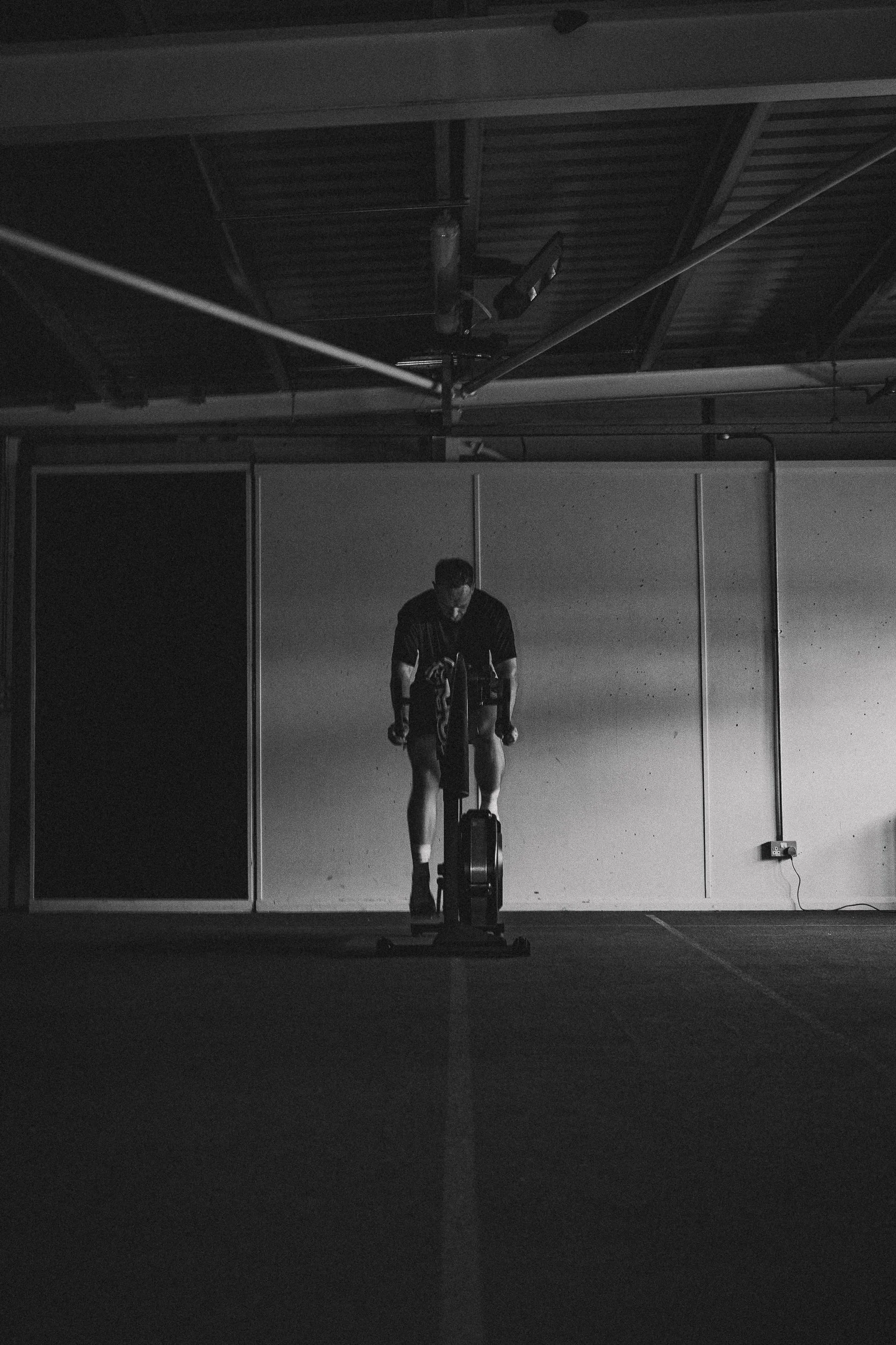 Silhouetted athlete training on an exercise bike in a dark gym for the Torra Performance Lilleshall campaign