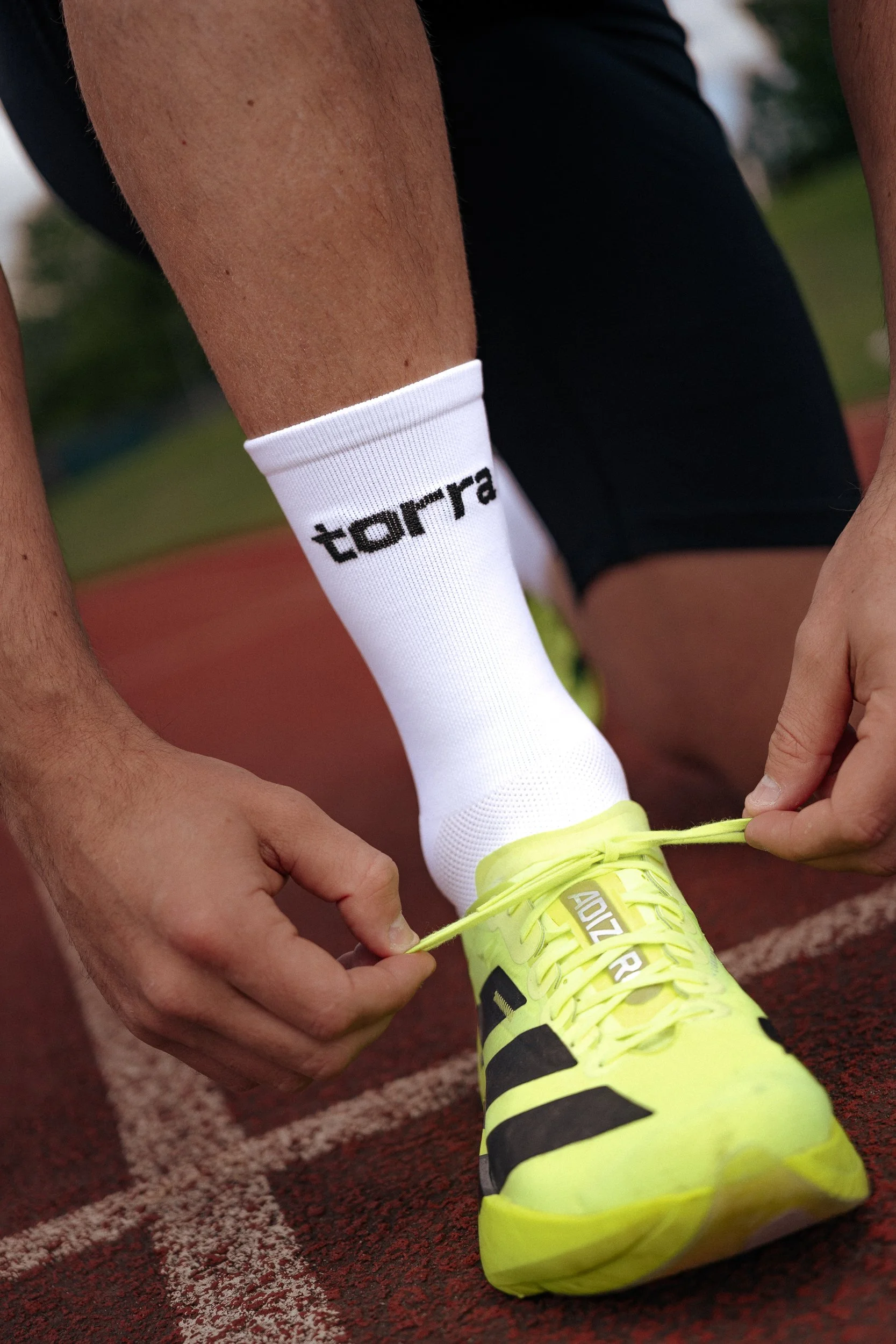 Athlete tying yellow running shoes wearing Torra branded socks on the track, Torra Performance Mens Health campaign