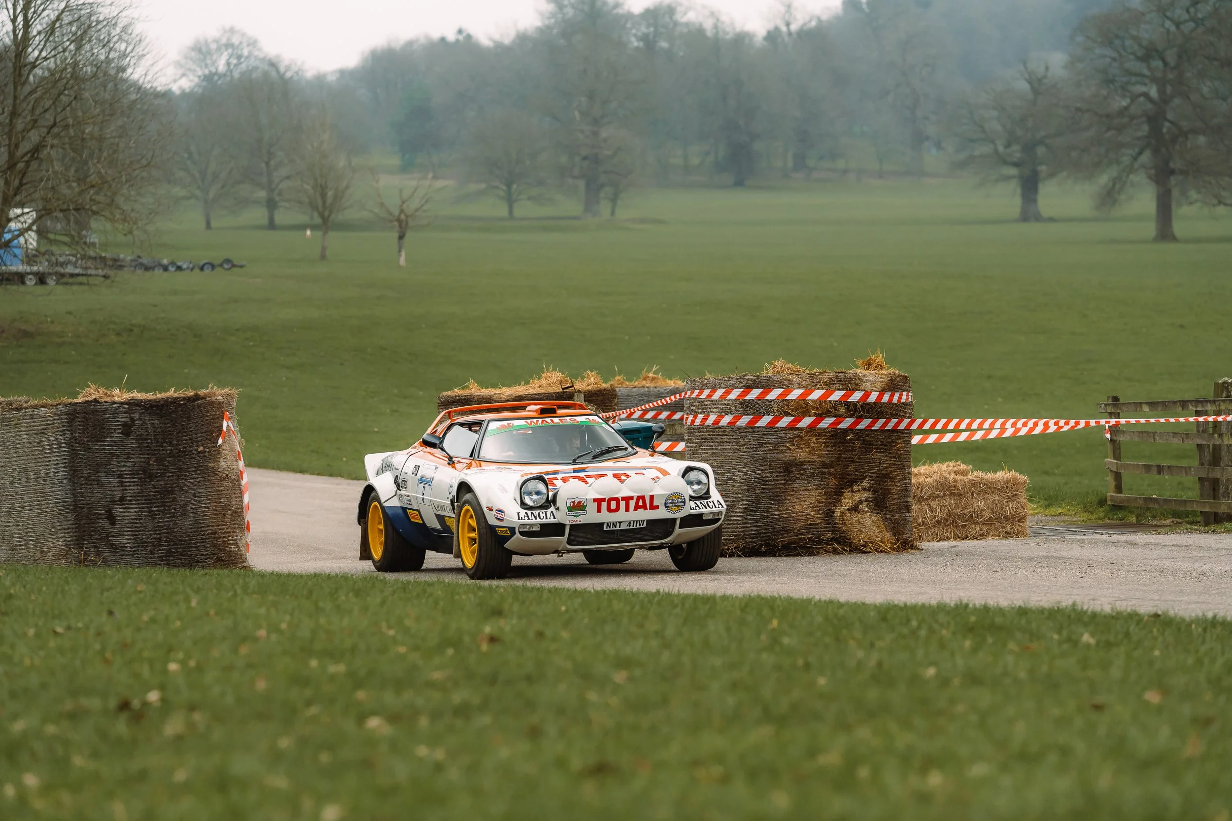 White Lancia Stratos rally car navigating a hay-bale-lined course at the Lombard Rally Festival