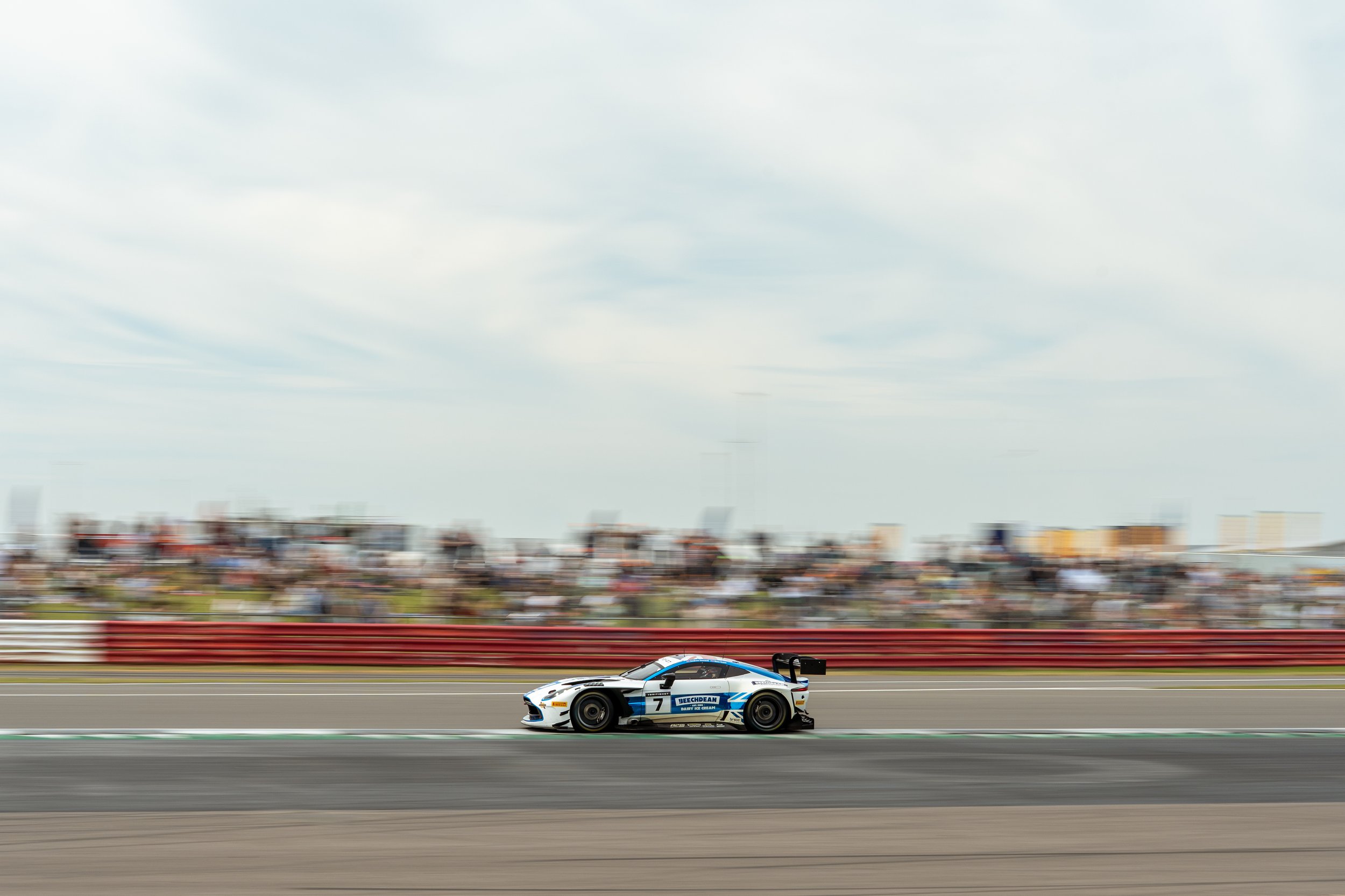 A race car on a racetrack with blurred background of buildings and sky.