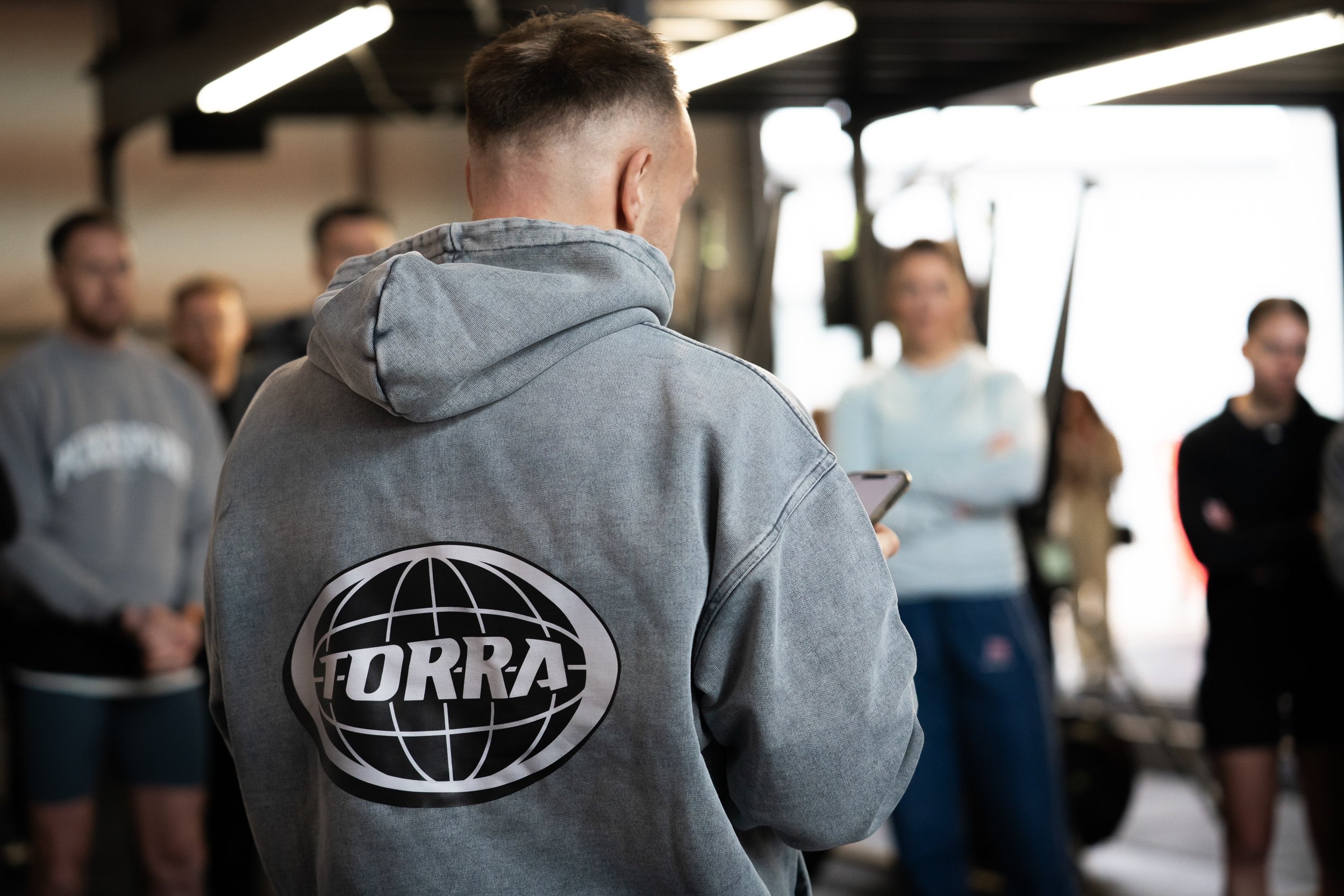 Back view of a person wearing a grey Torra branded hoodie inside a gym for the Engine Series campaign