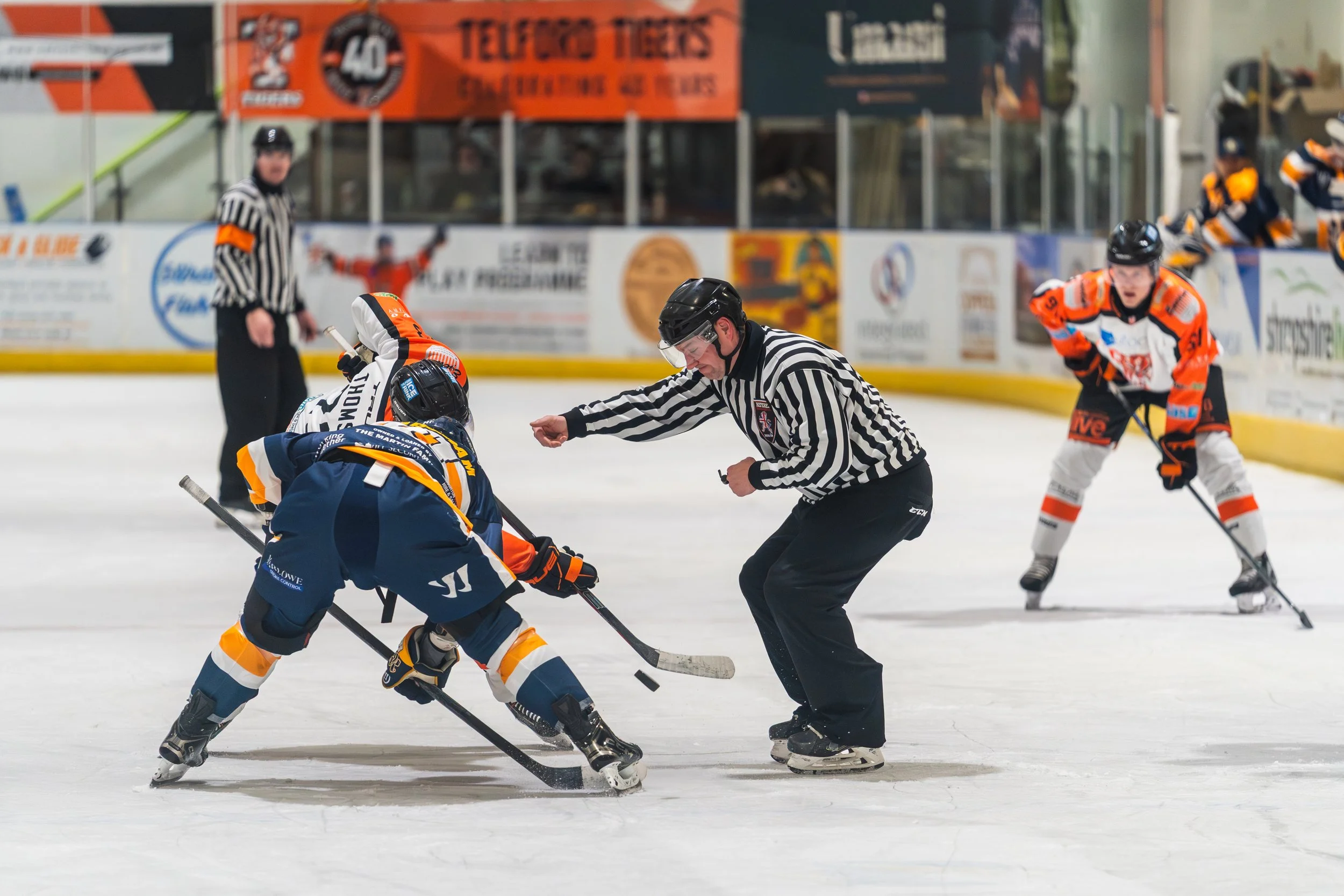 Hockey players face off on the ice with a referee overseeing the game.