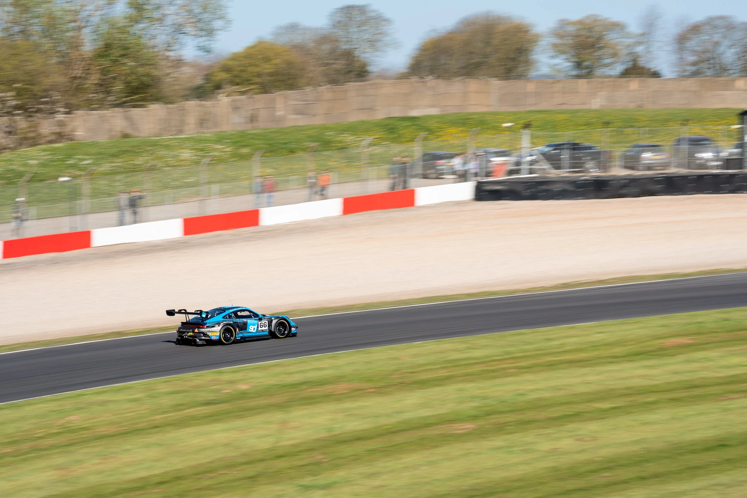 Blue race car with the number 66 on its side on a racetrack, speeding along the asphalt with motion blur in the foreground and background.