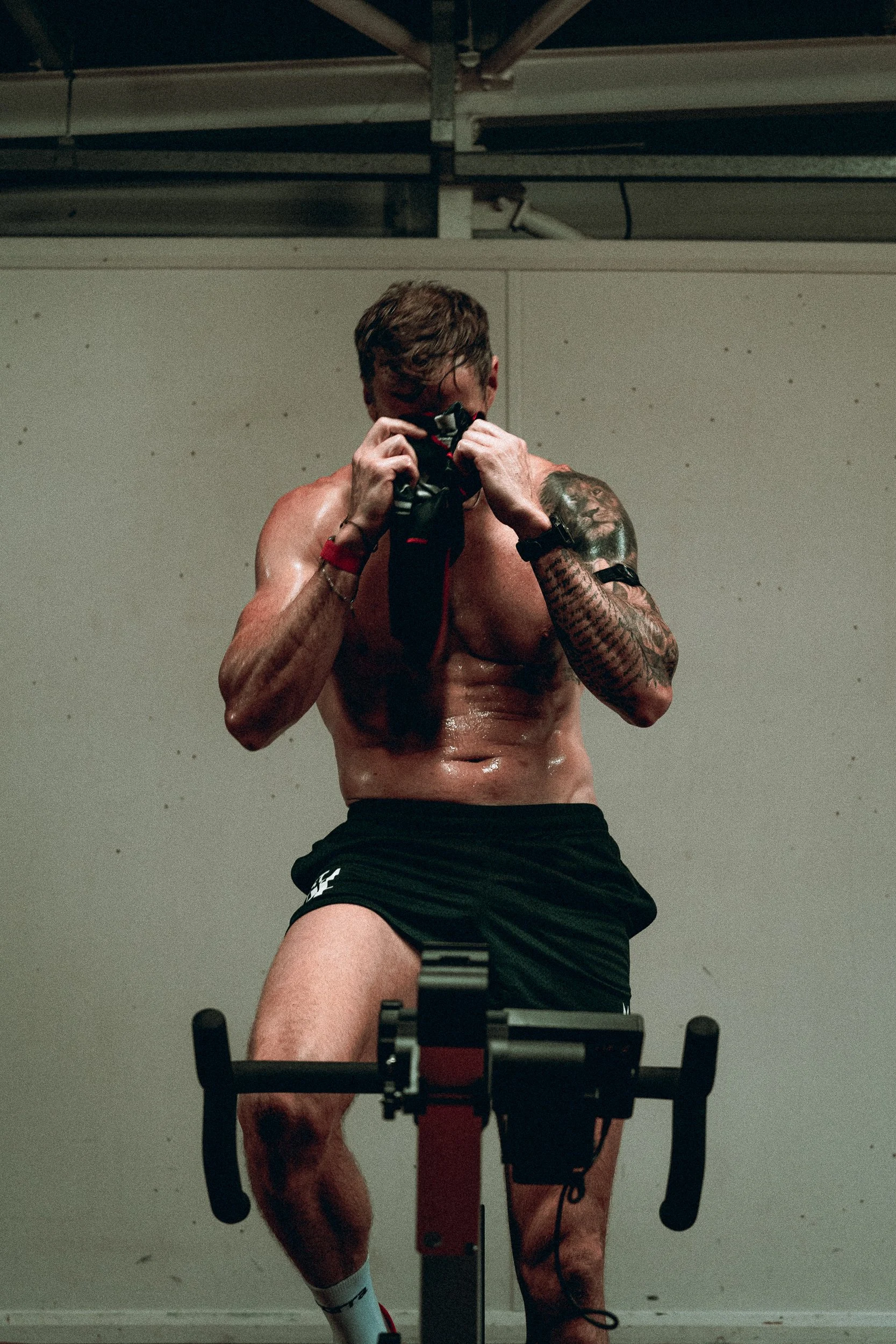 Shirtless athlete gripping the handlebars mid-effort on an exercise bike for the Torra Performance Lilleshall campaign