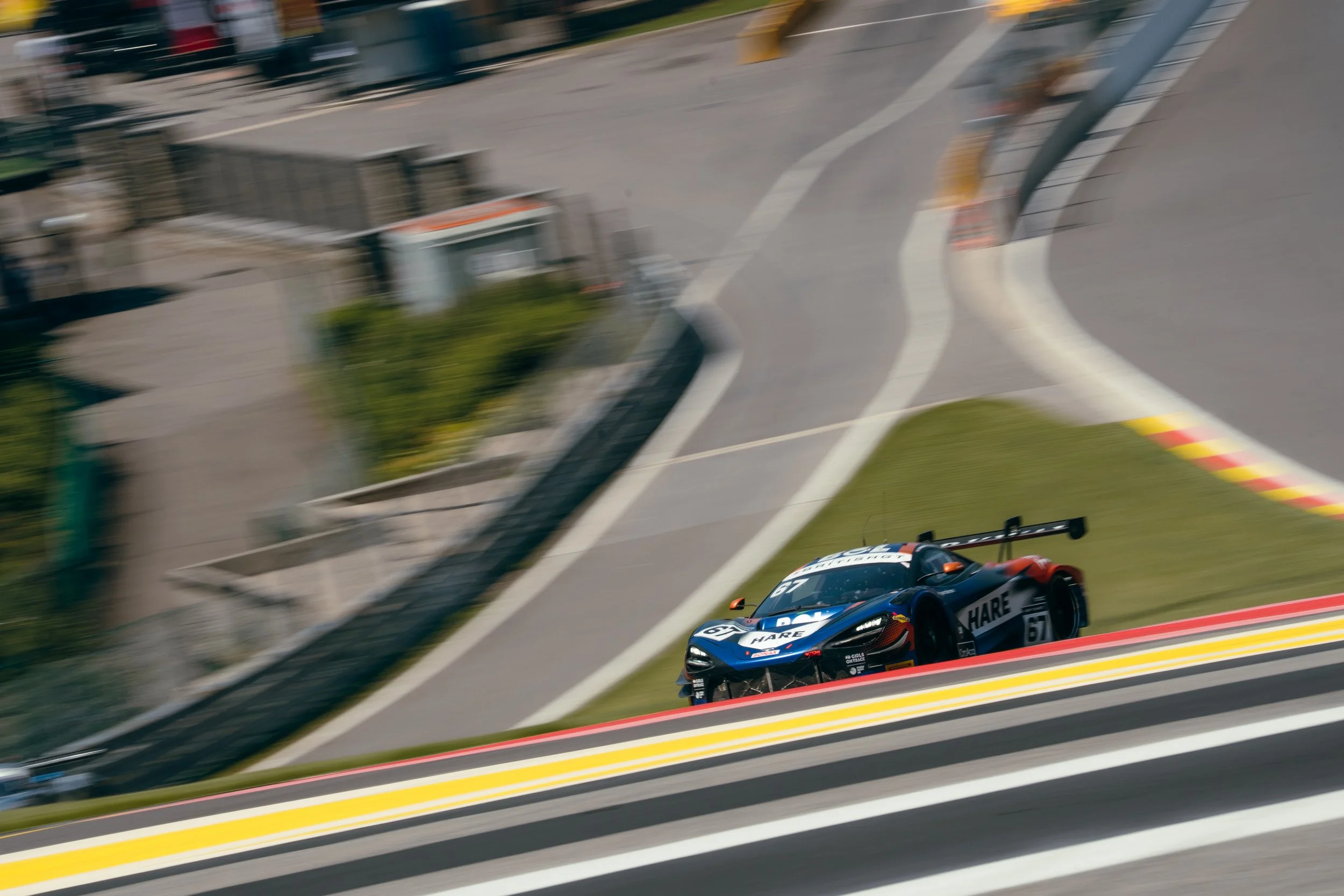 A race car speeding on a track with blurred background, with a curved section and safety barriers visible.
